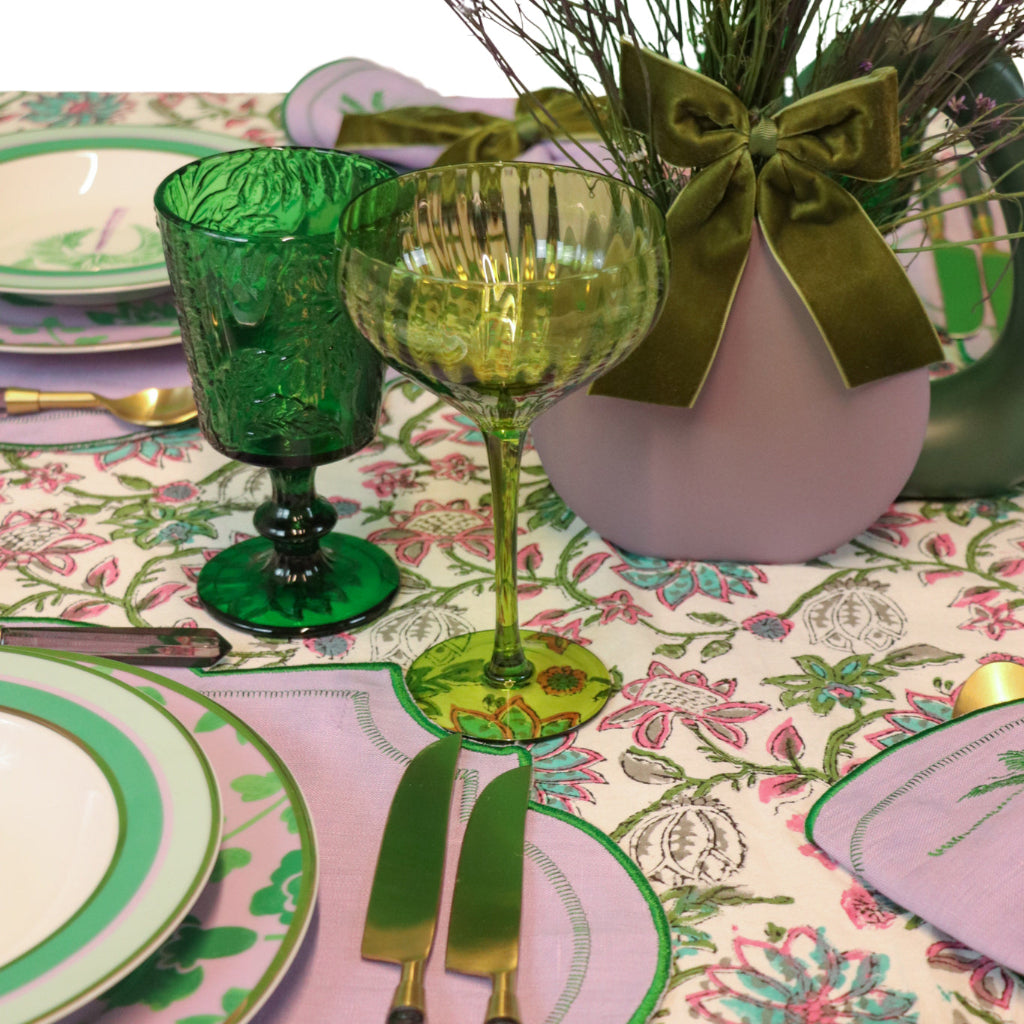 Decorative table setting with green glassware, pink plates, and a floral tablecloth.