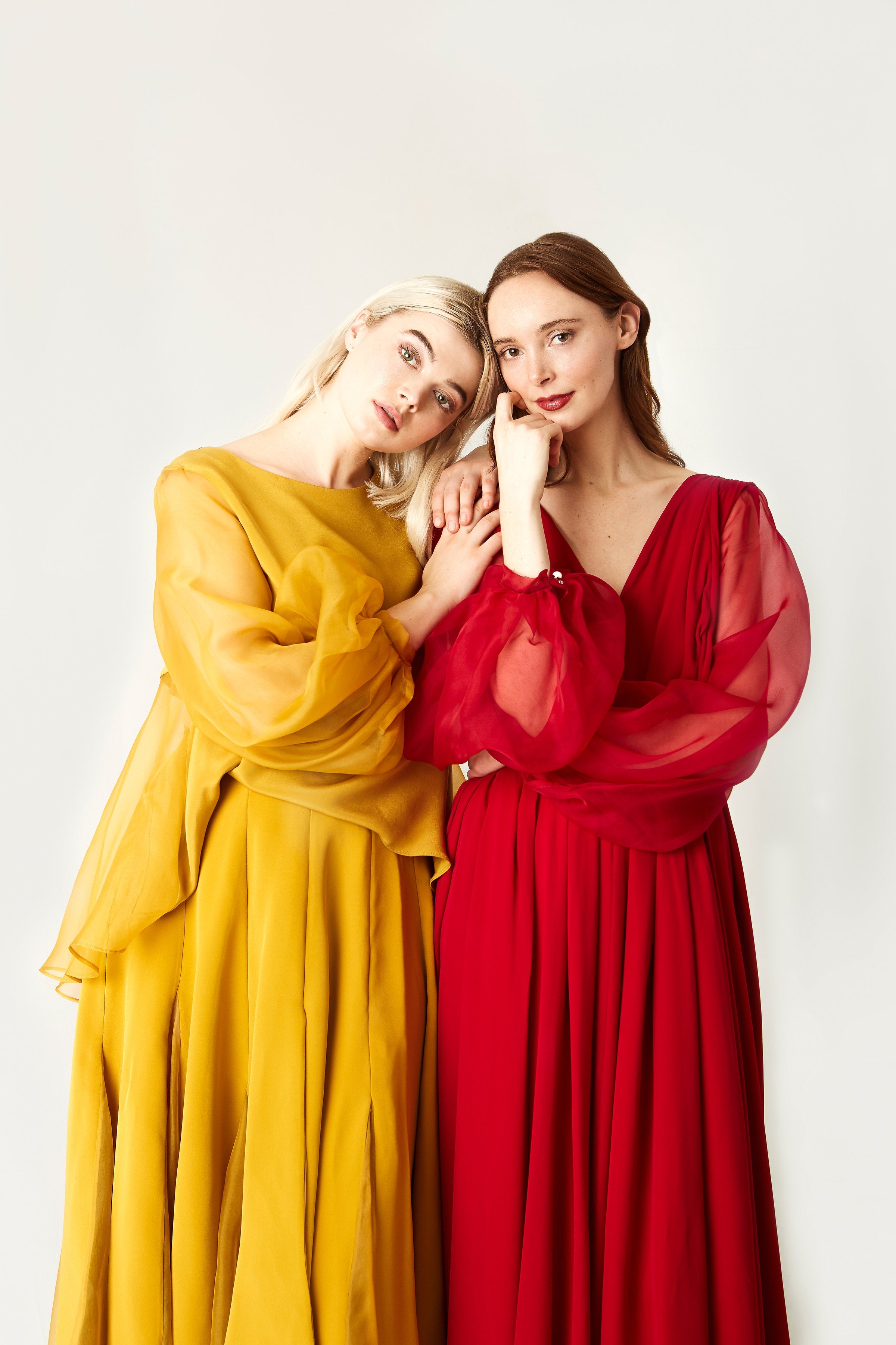 Two women in colorful dresses posing against a white background
