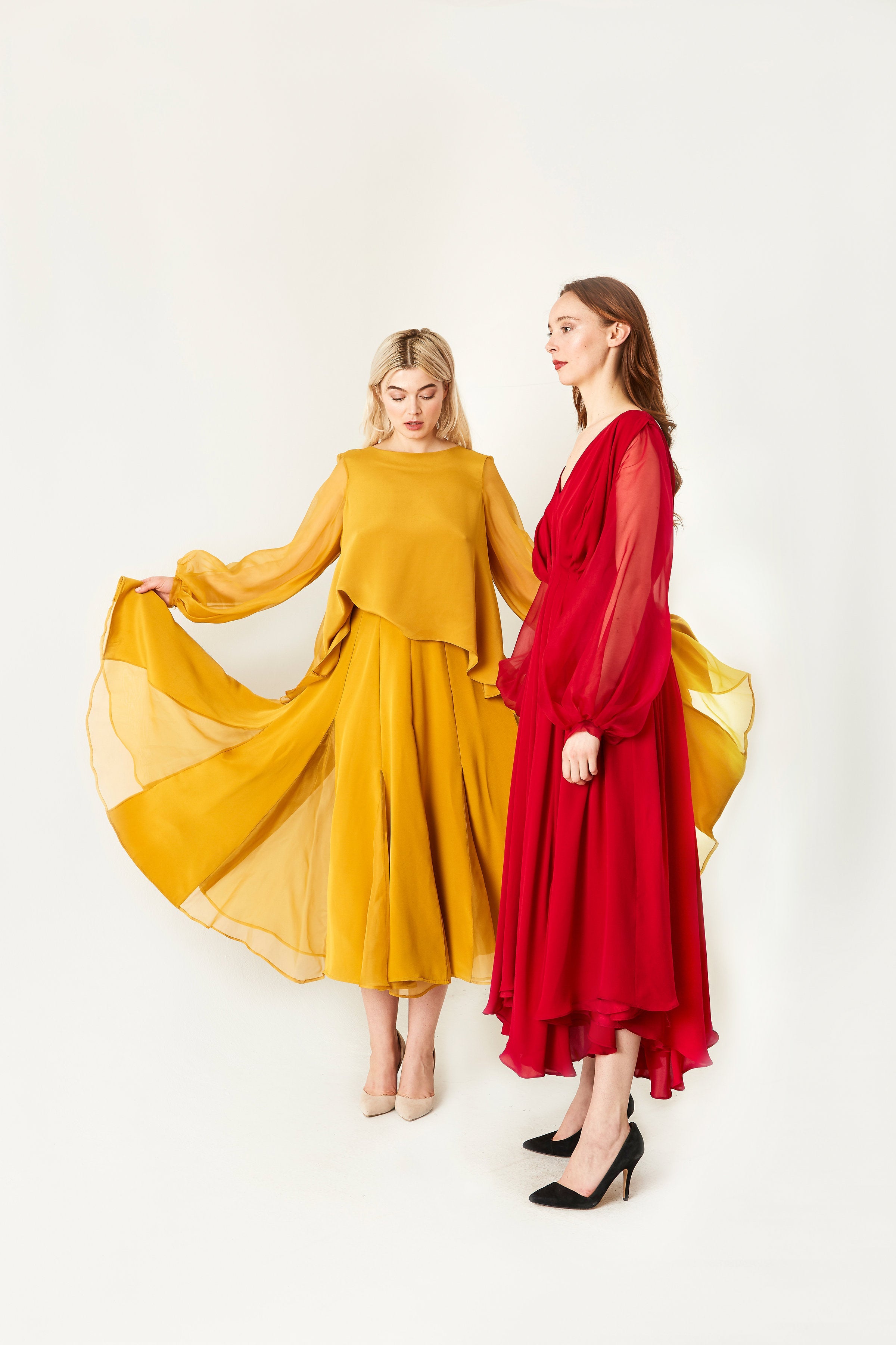Two women wearing mustard yellow and red dresses on a white background