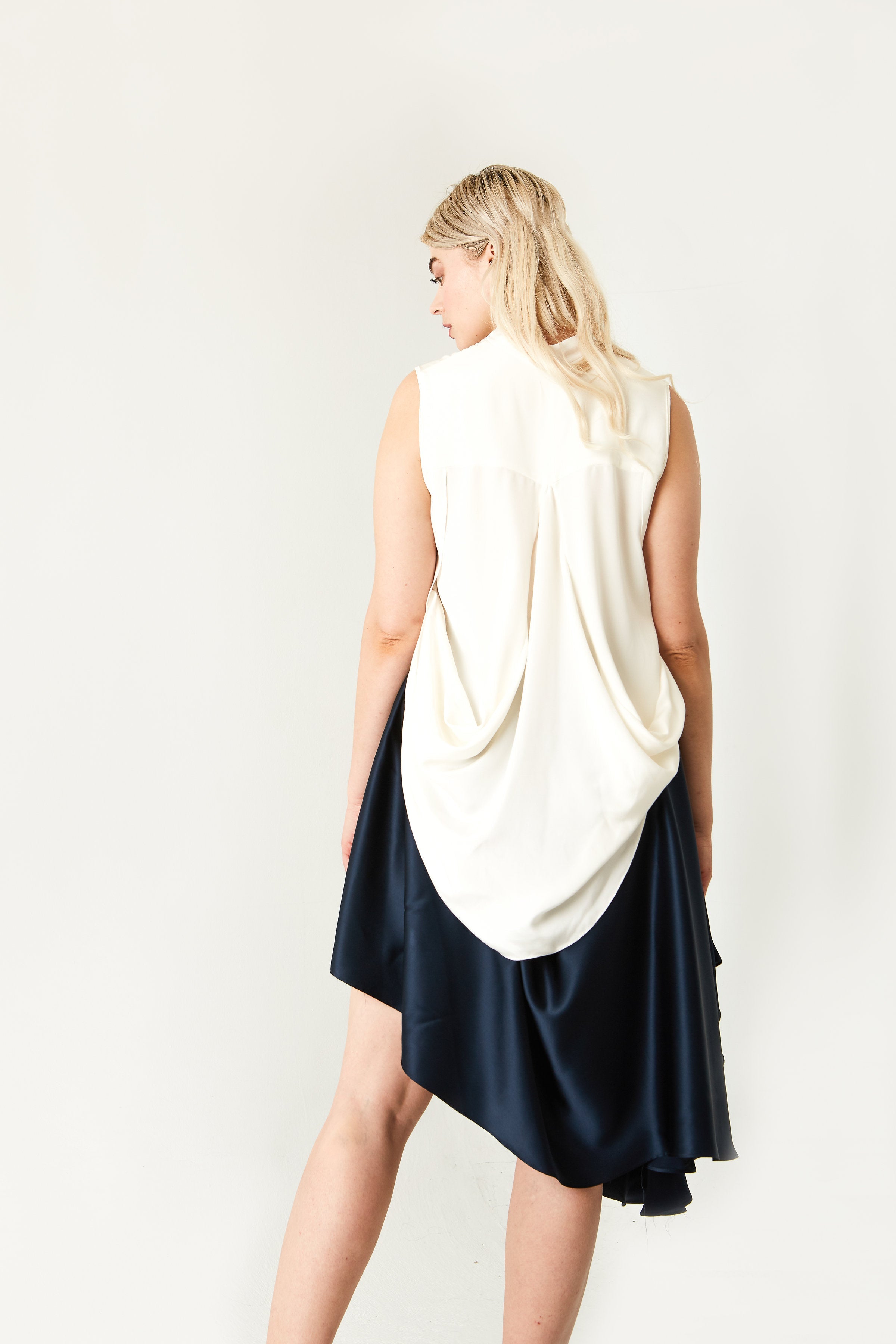 Woman wearing a two-tone dress with a white top and navy skirt on a plain background