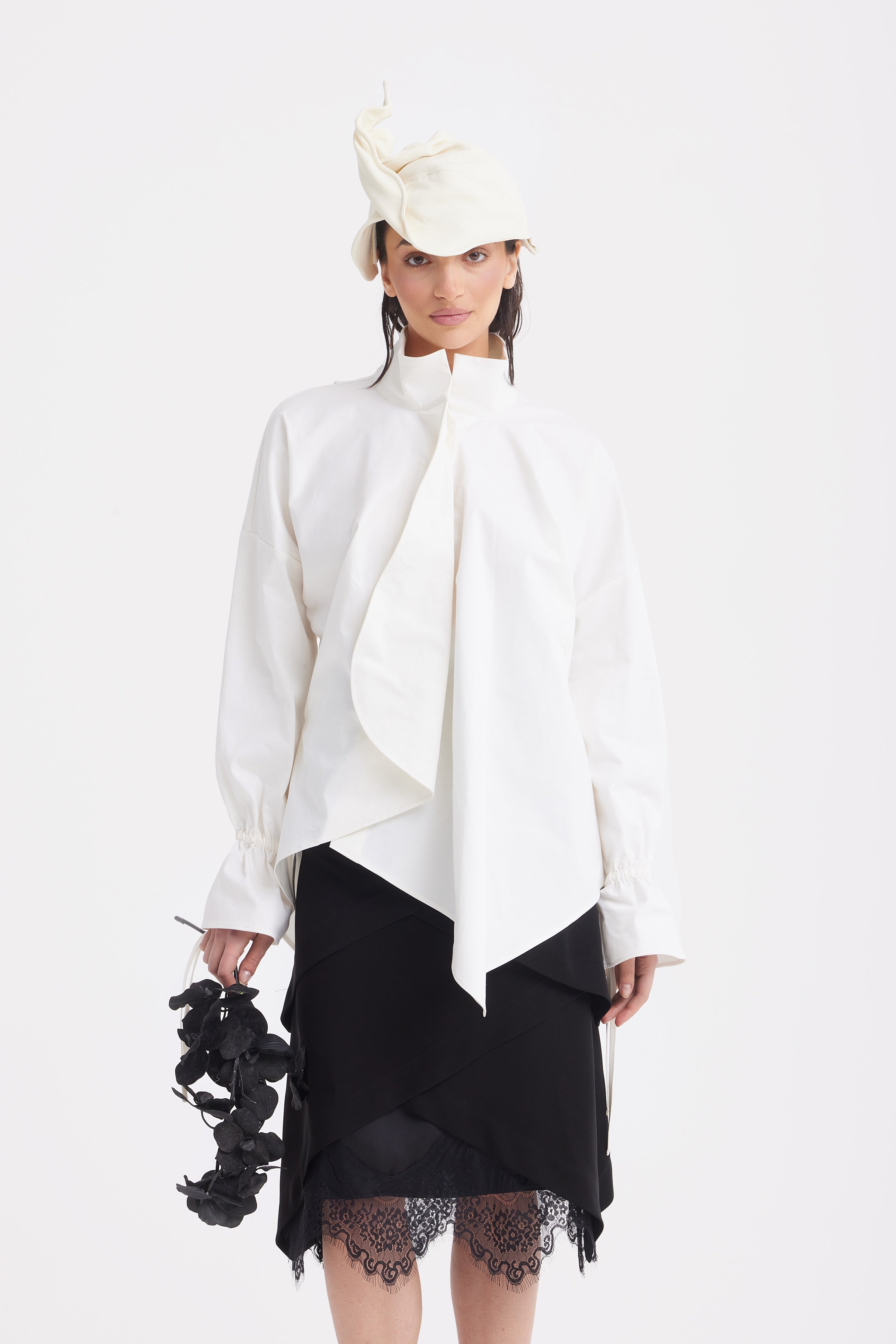 Woman wearing a white blouse with a black skirt with lace hem and a white hat on a white background