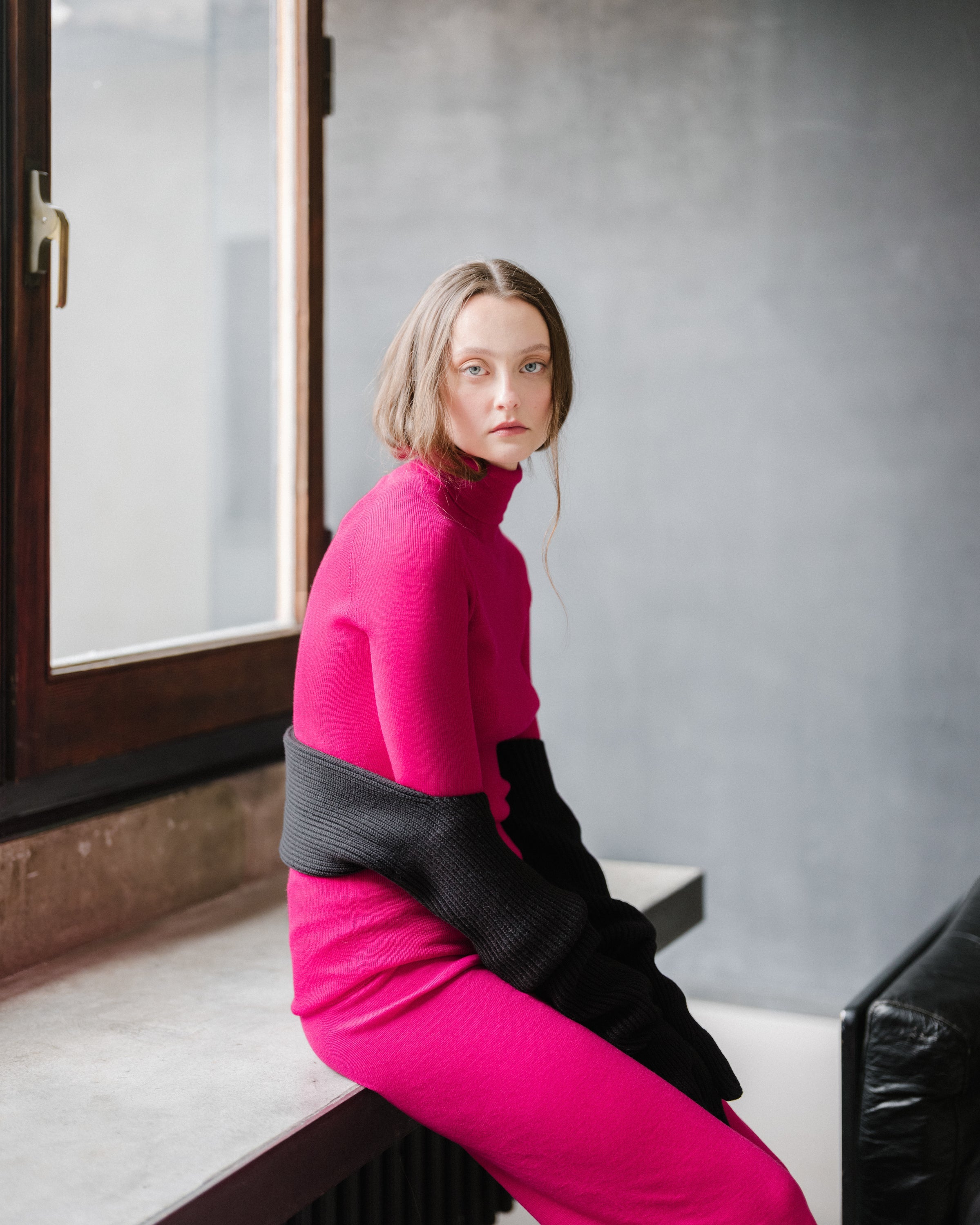 Person wearing a pink and black outfit sitting on a windowsill.