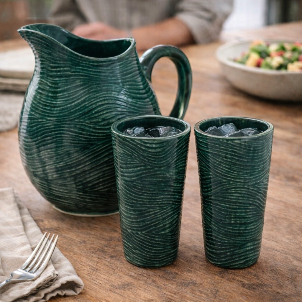 Green ceramic pitcher and two glasses on a wooden table with a blurred background