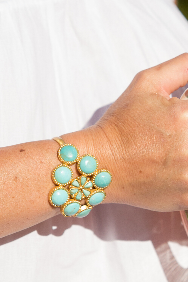 Hand wearing a turquoise and gold bracelet on a white background
