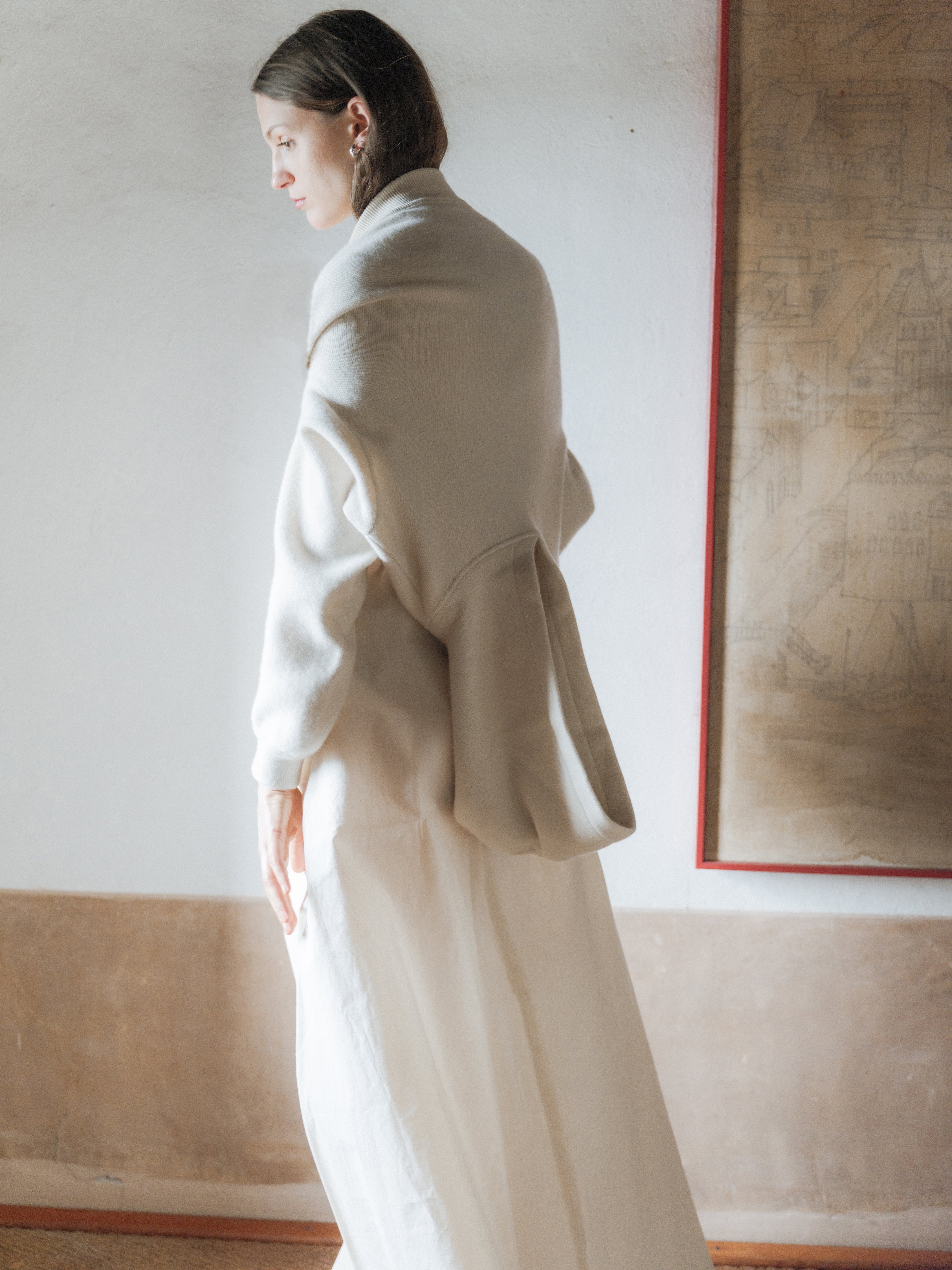 Woman wearing an upside down light-colored hoodie in a room with a painting on the wall.