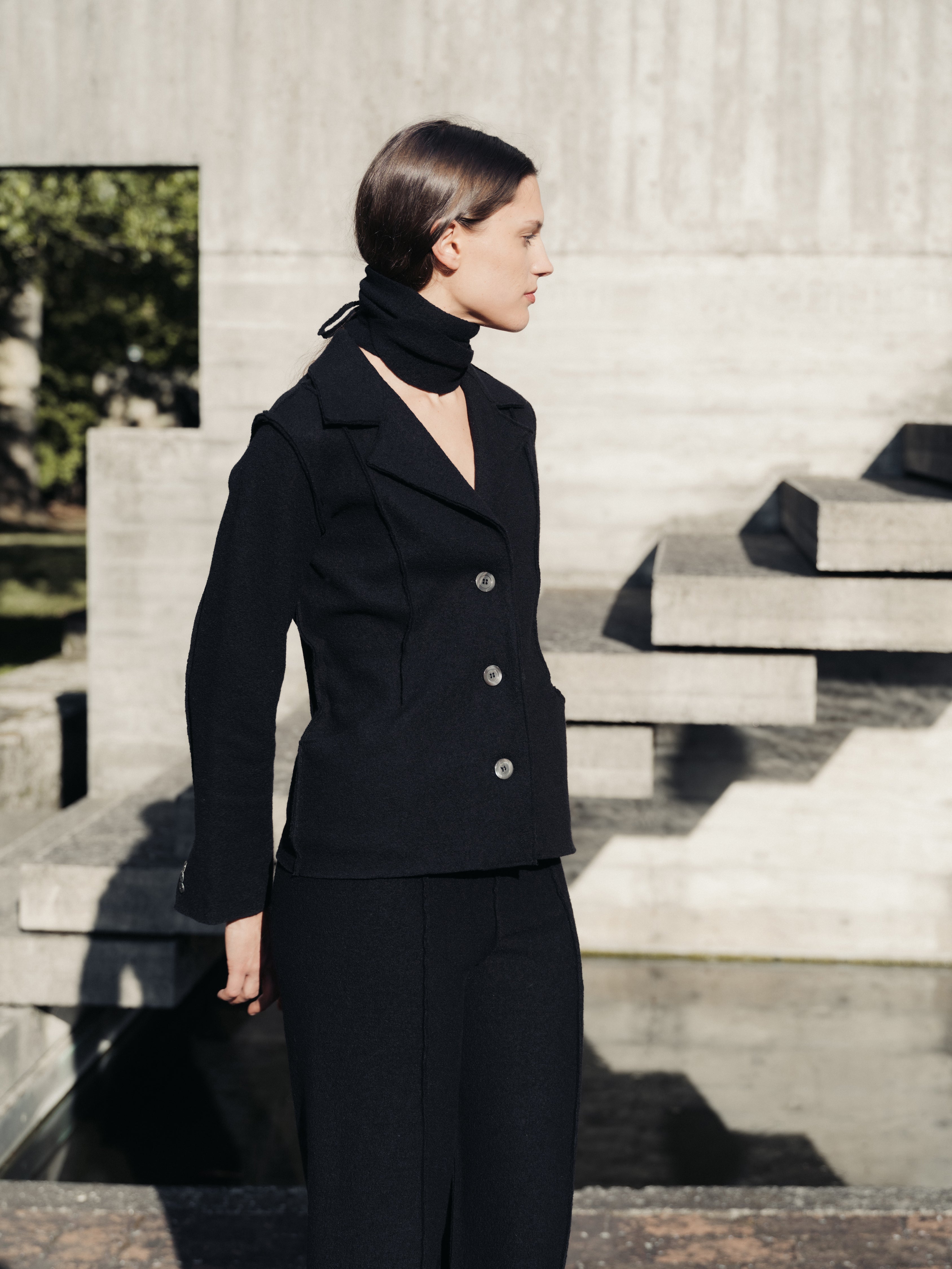 Woman in a black outfit standing outdoors on stone steps.
