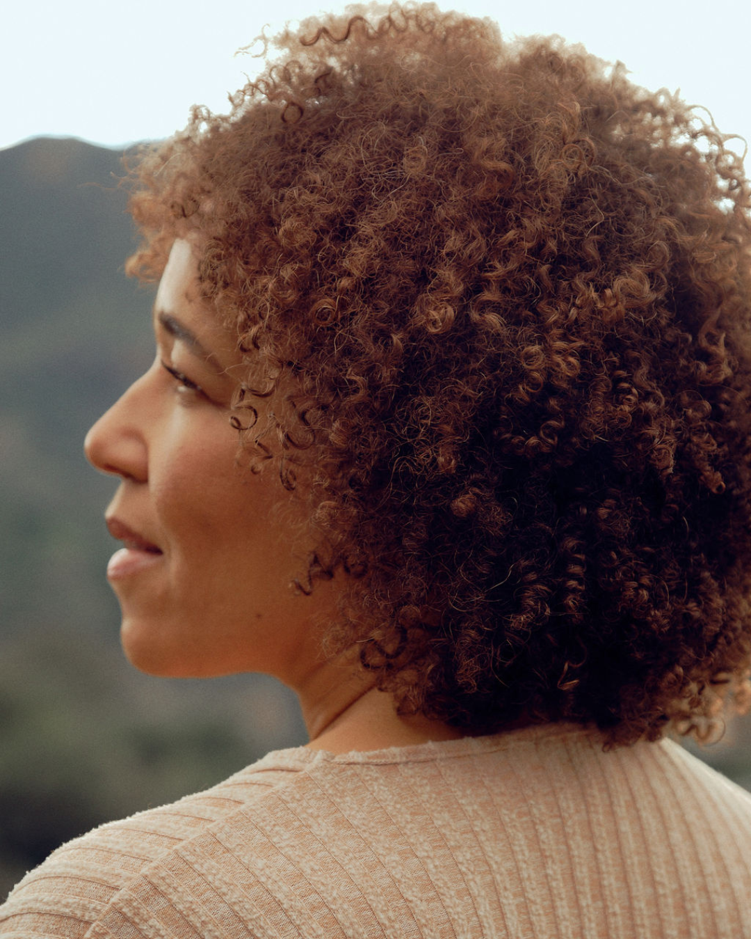 Woman with curly hair looking into the distance with mountains in the background