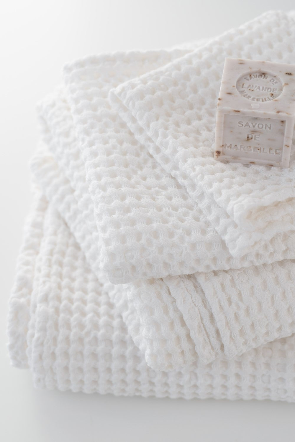 Folded white textured blanket with a brand tag on a light gray background