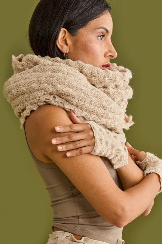 Woman wearing a beige knitted scarf against a green background