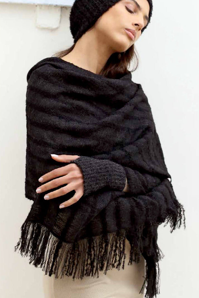 Woman wearing a black fringed scarf and beanie against a white background