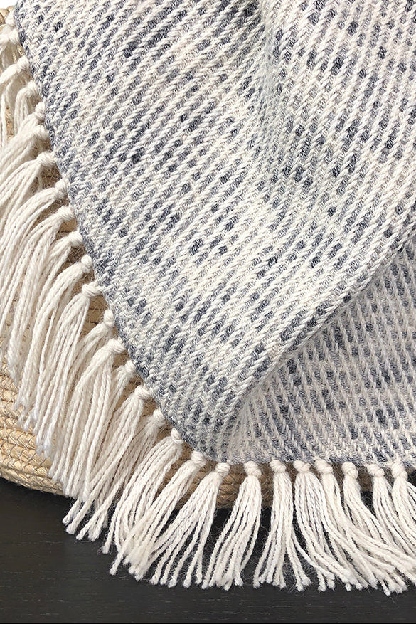 Textured blanket with fringe draped over a woven basket on a black surface.