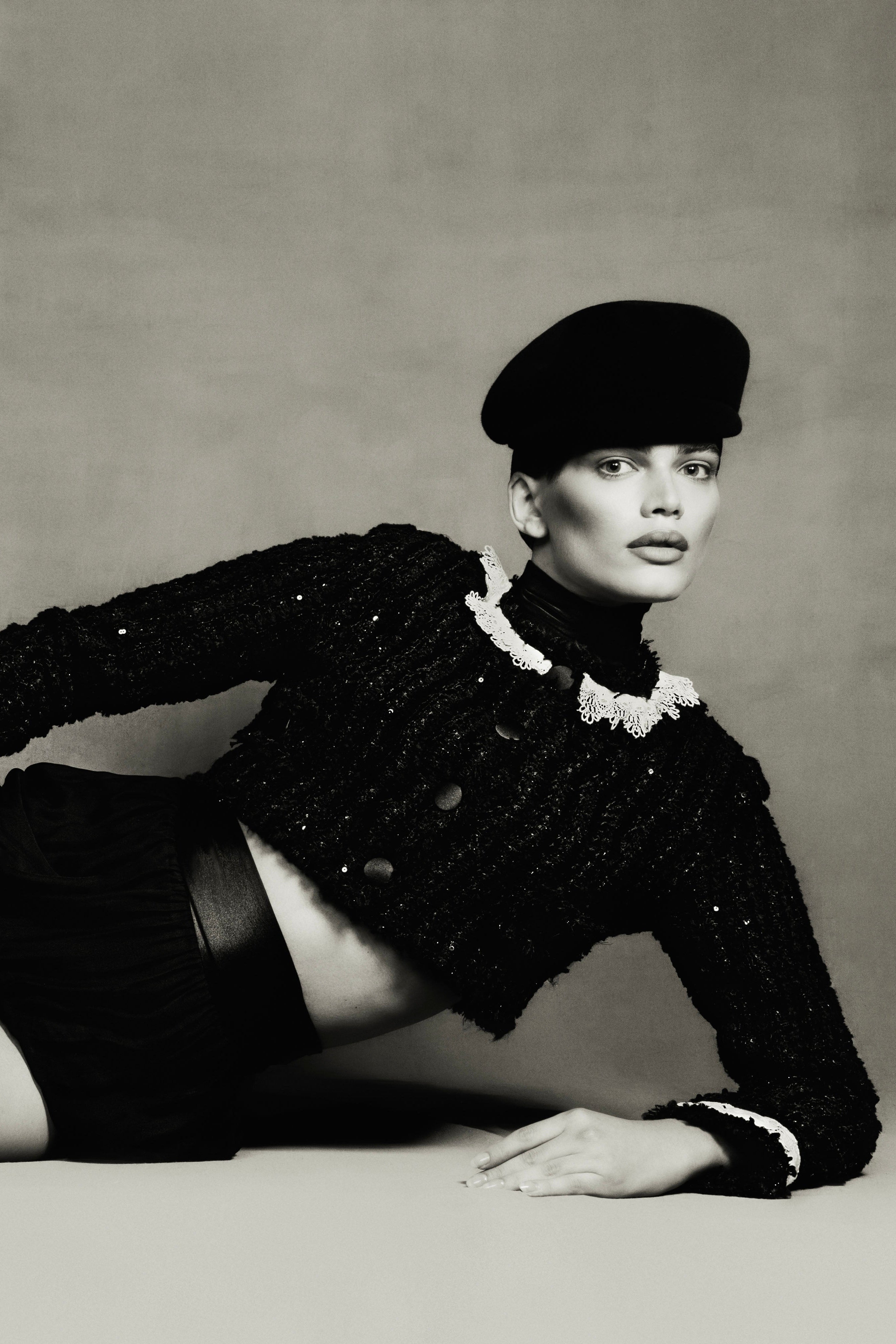 Black and white portrait of a model wearing a textured sweater and beret against a plain background