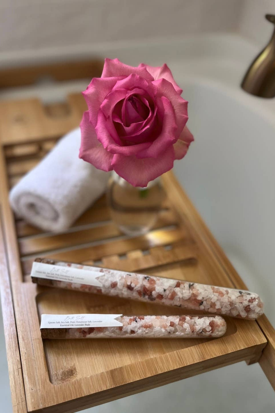 Bath tray with bath bombs, towel, and pink rose on a bathtub.