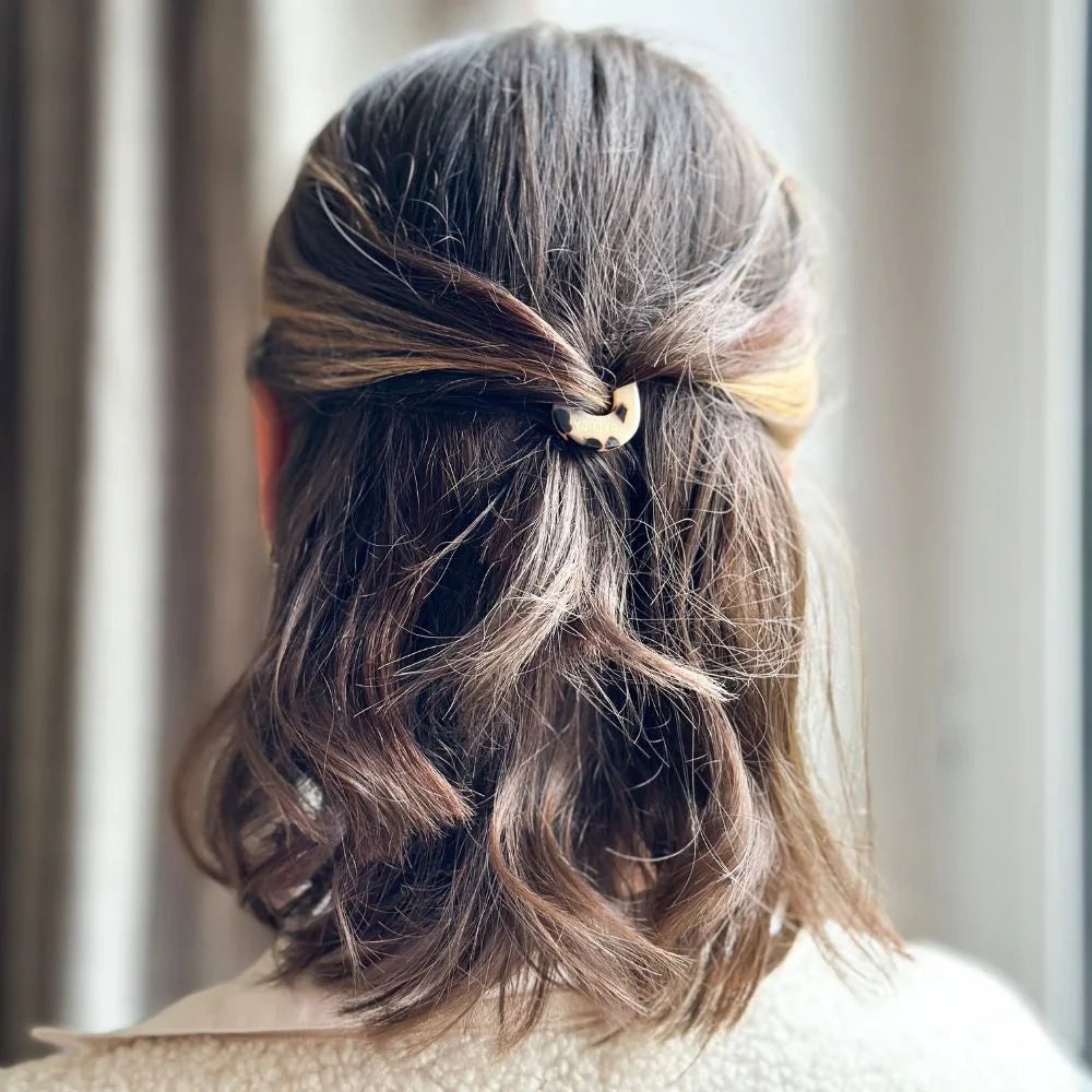 Close-up of a person's hair styled with a hair tie against a neutral background