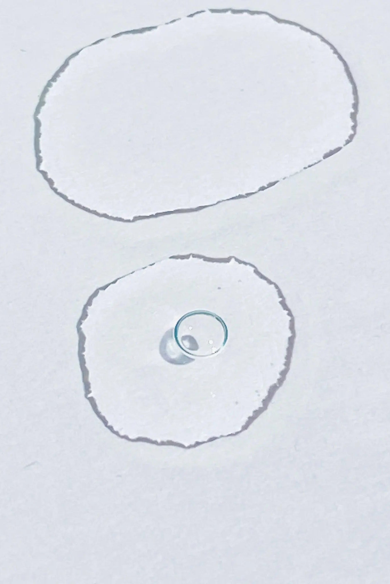 Two drops of Barcola Azzurro Mare Replenishing Elixir with Hyaluronic acid on a white surface.