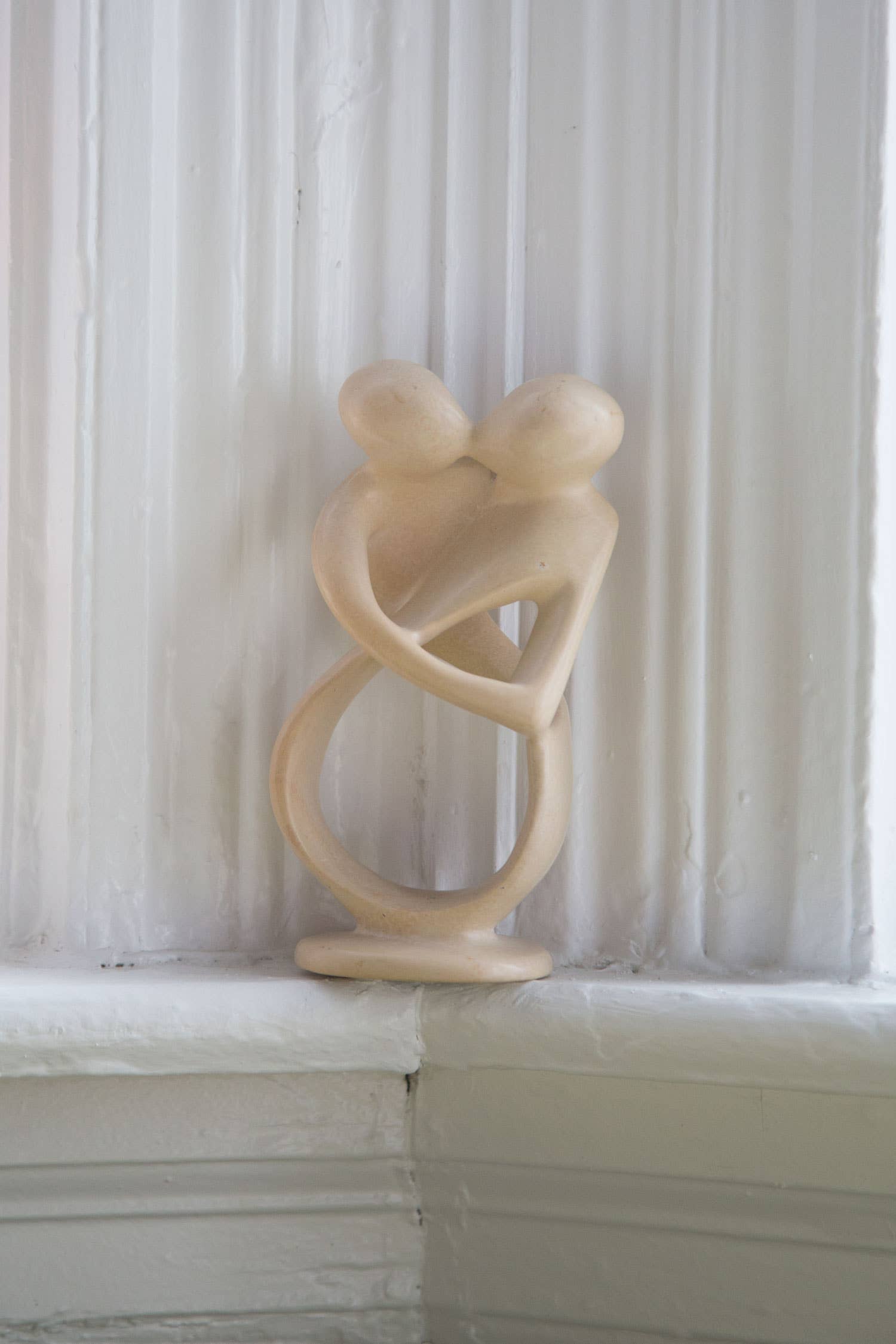 Abstract sculpture of two intertwined figures on a white surface with a textured white wall background