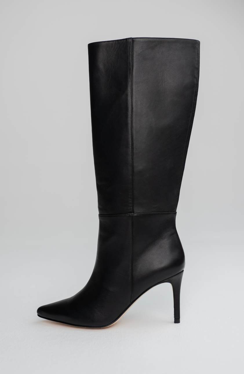 A single black leather knee-high boot with a pointed toe and slim high heel, photographed against a light gray studio background.