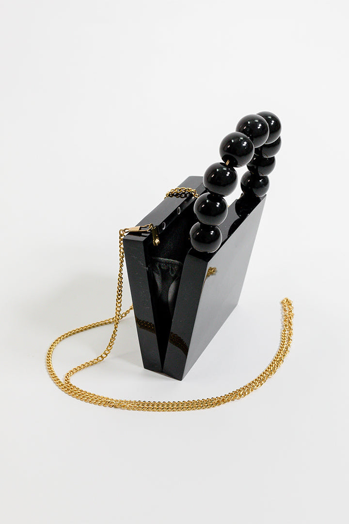 Black handbag with gold chain and black beads on a white background