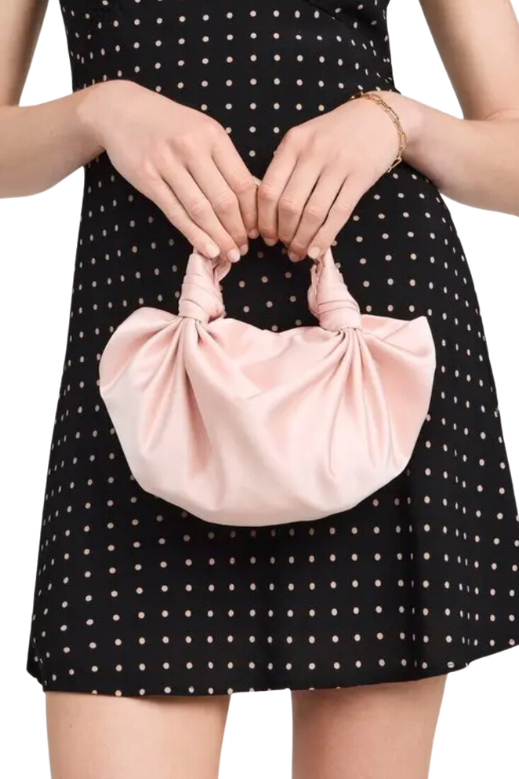 Person holding a pink handbag with a black polka dot dress on a white background