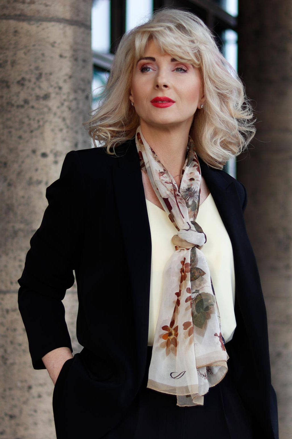 Woman wearing a black blazer and floral scarf against a stone wall background