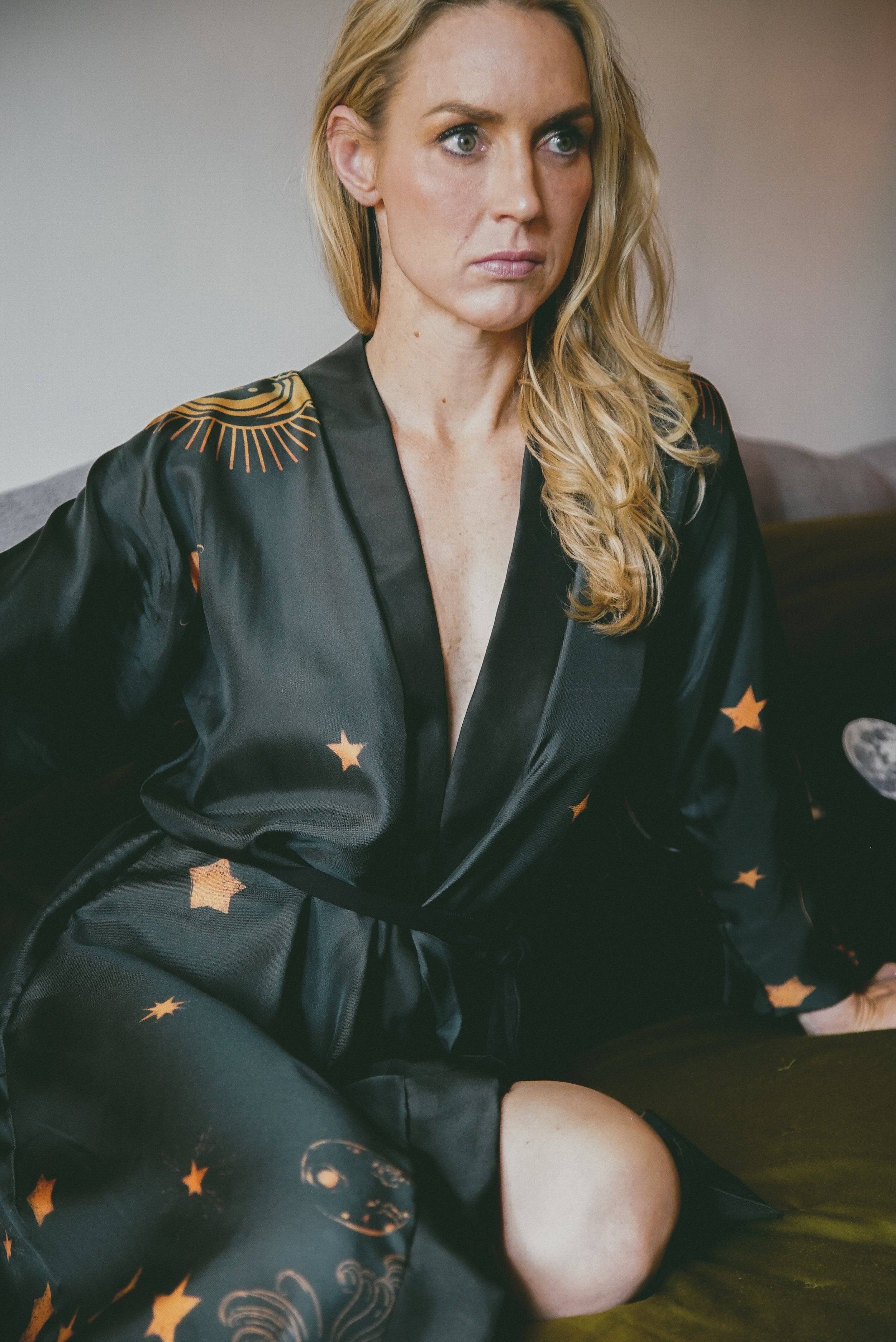 Woman wearing a black satin robe with star patterns sitting on a couch.