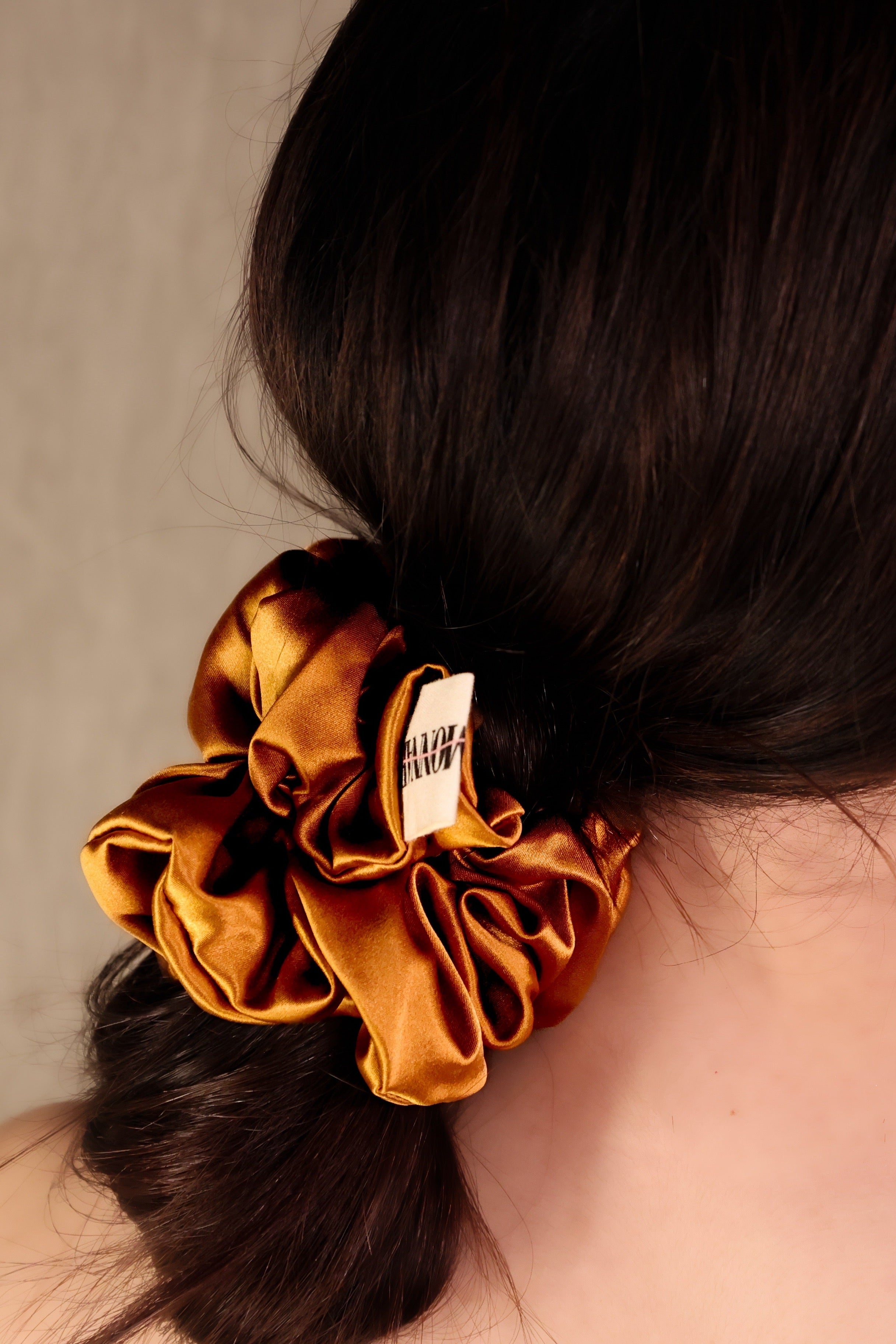 Woman with a gold scrunchie in her hair against a neutral background