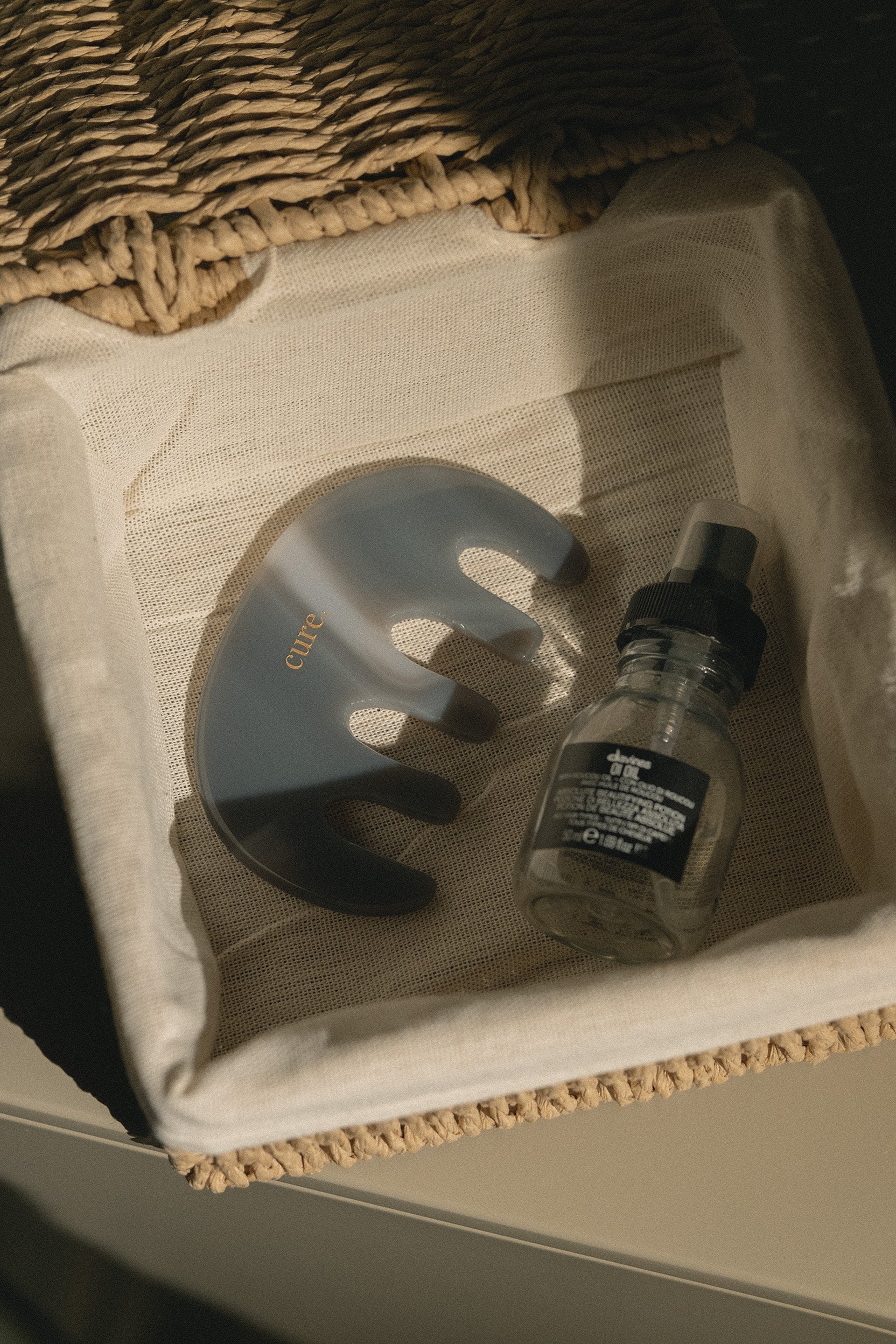 A clear silicone nail care tool with gold lettering, placed next to a small glass dropper bottle with a black cap inside a beige fabric-lined tray.