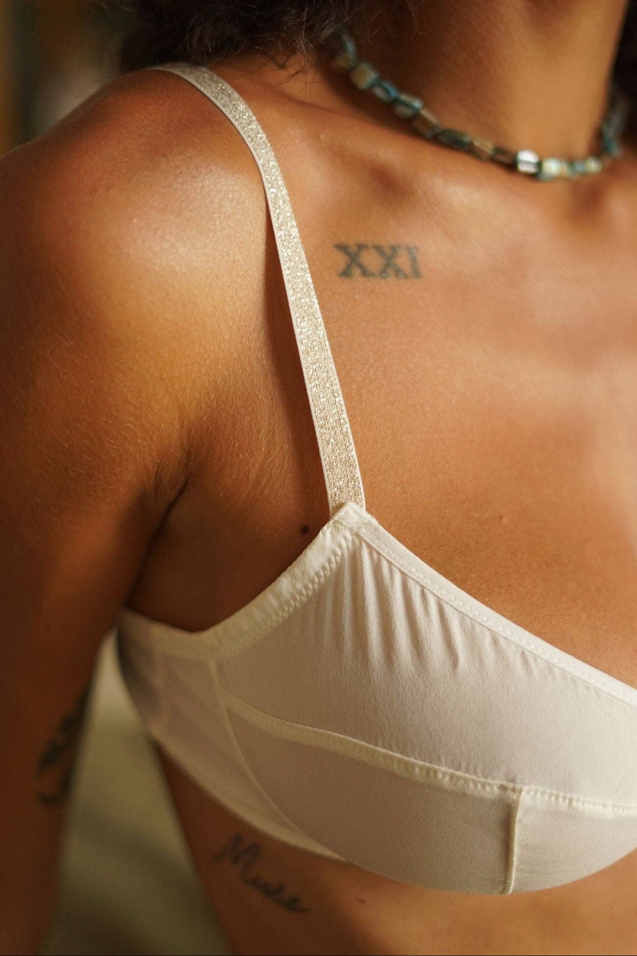 Close-up of a person wearing a beige bralette with tattoos visible on the skin.