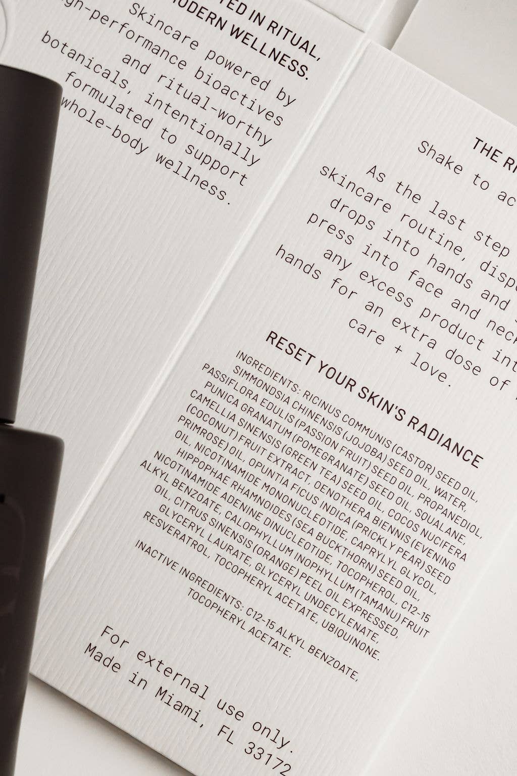 An open booklet or recipe card with printed skincare instructions and ingredient lists, photographed on a white surface with part of a black object visible at the left edge.