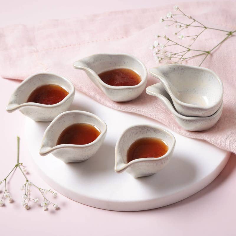 Set of ceramic condiment dishes with a liquid inside on a pink surface.