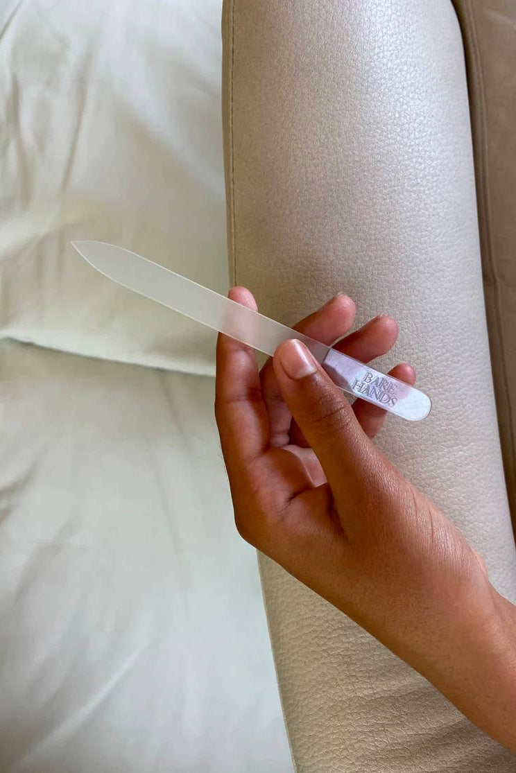 Hand holding a glass nail file against a white background
