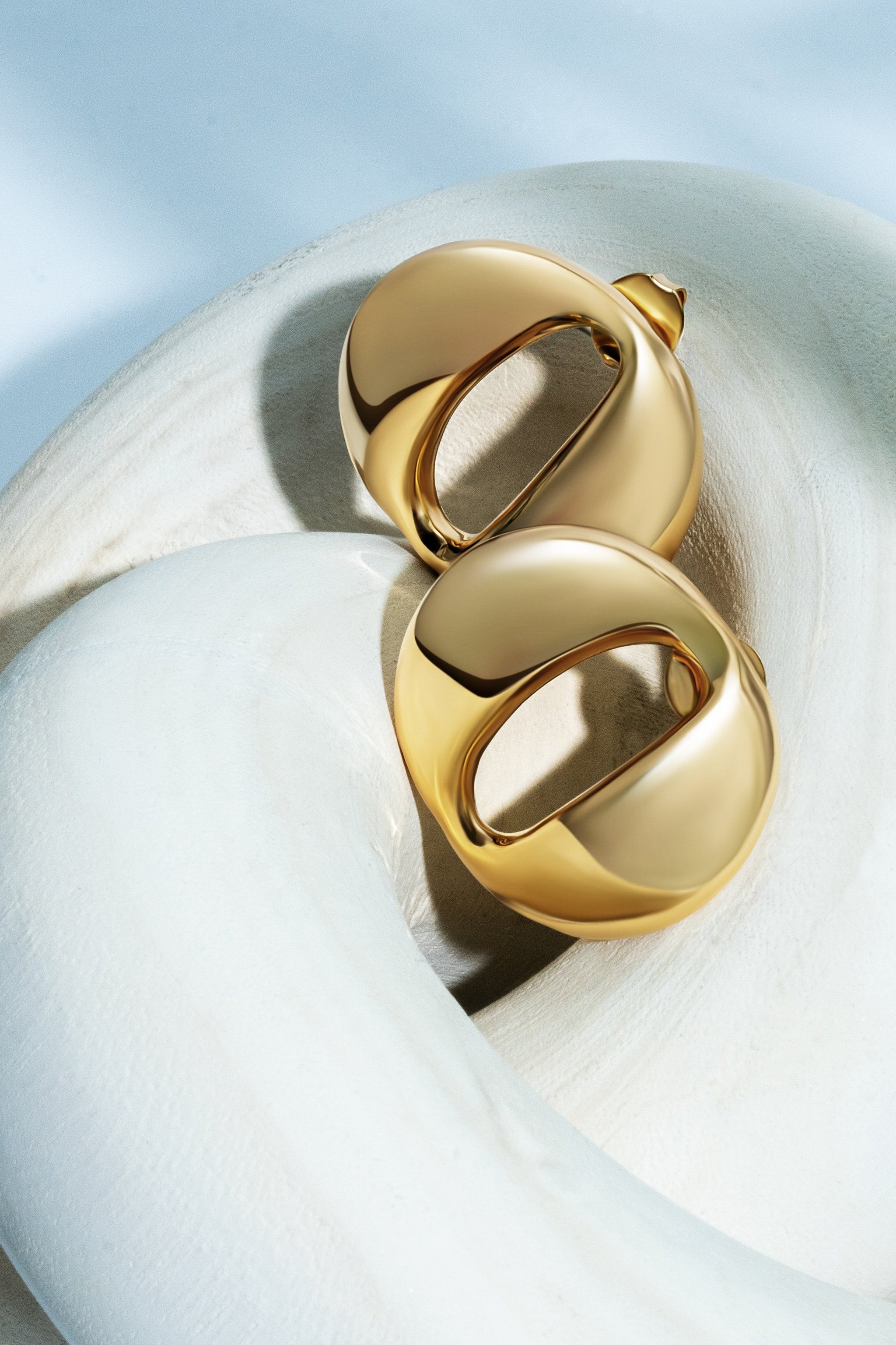 Gold earrings on a white surface with a light blue background