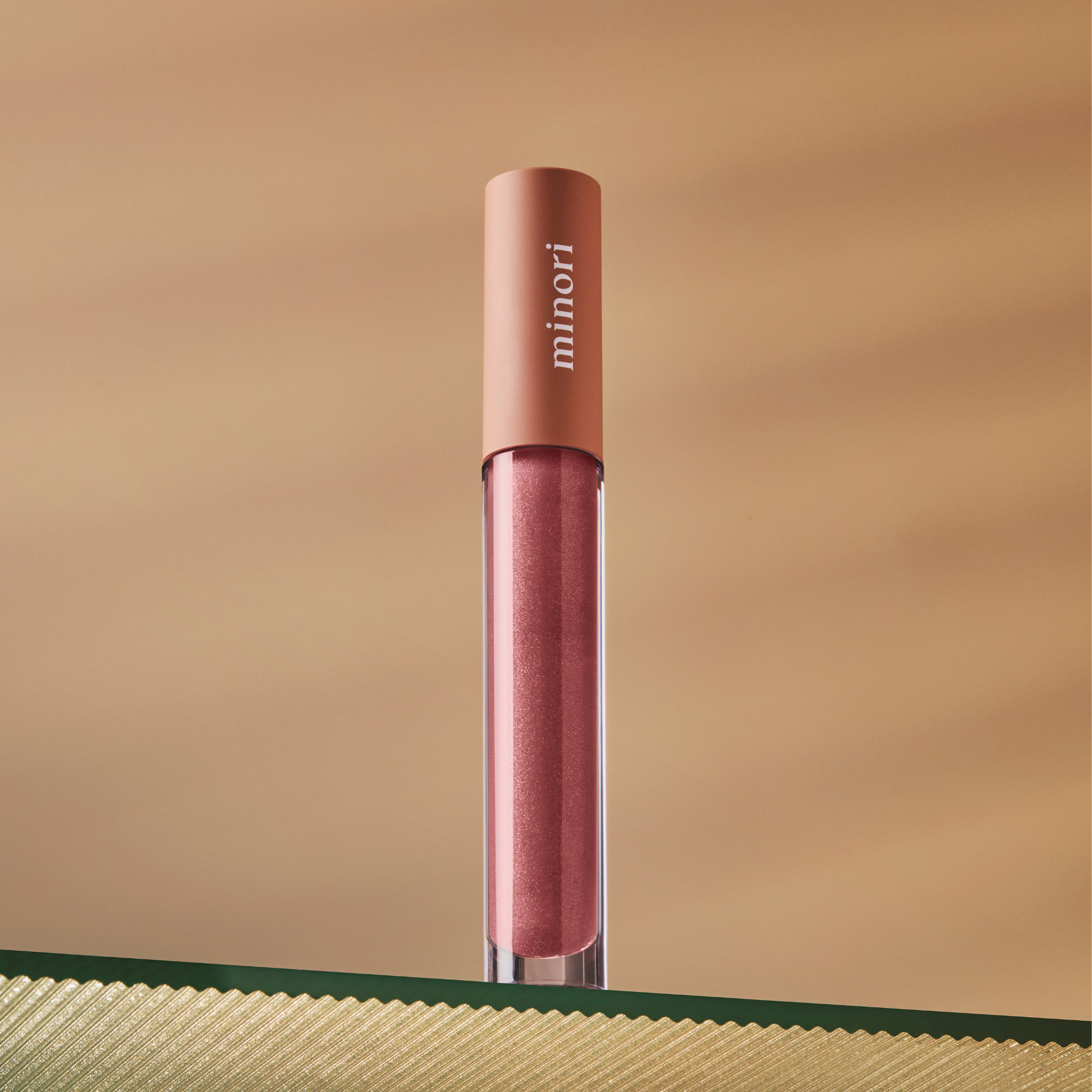 A tube of pink lip gloss with the brand name 'Minori' written on the cap, displayed against a beige background.