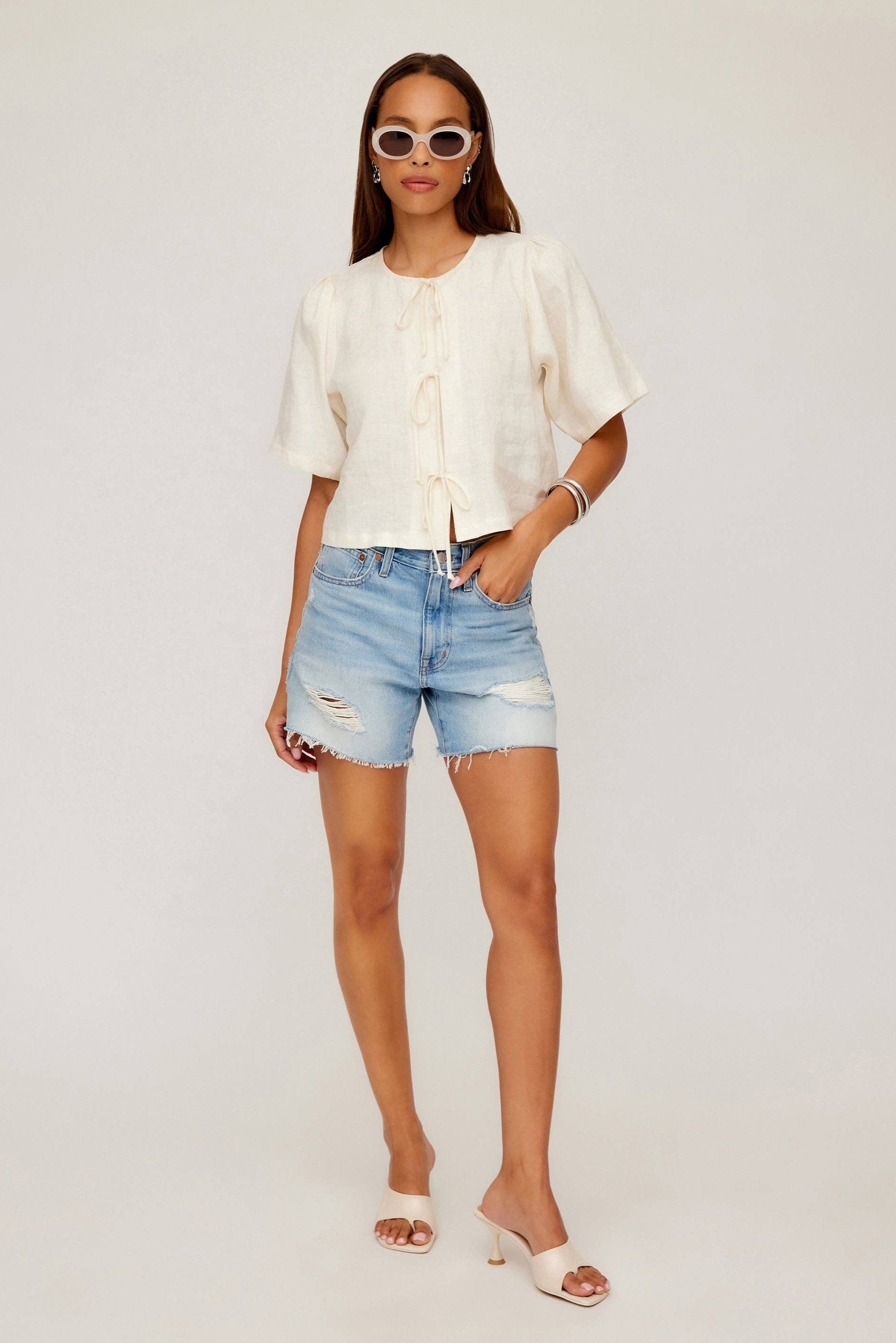 Woman wearing a white blouse and light blue denim shorts on a white background