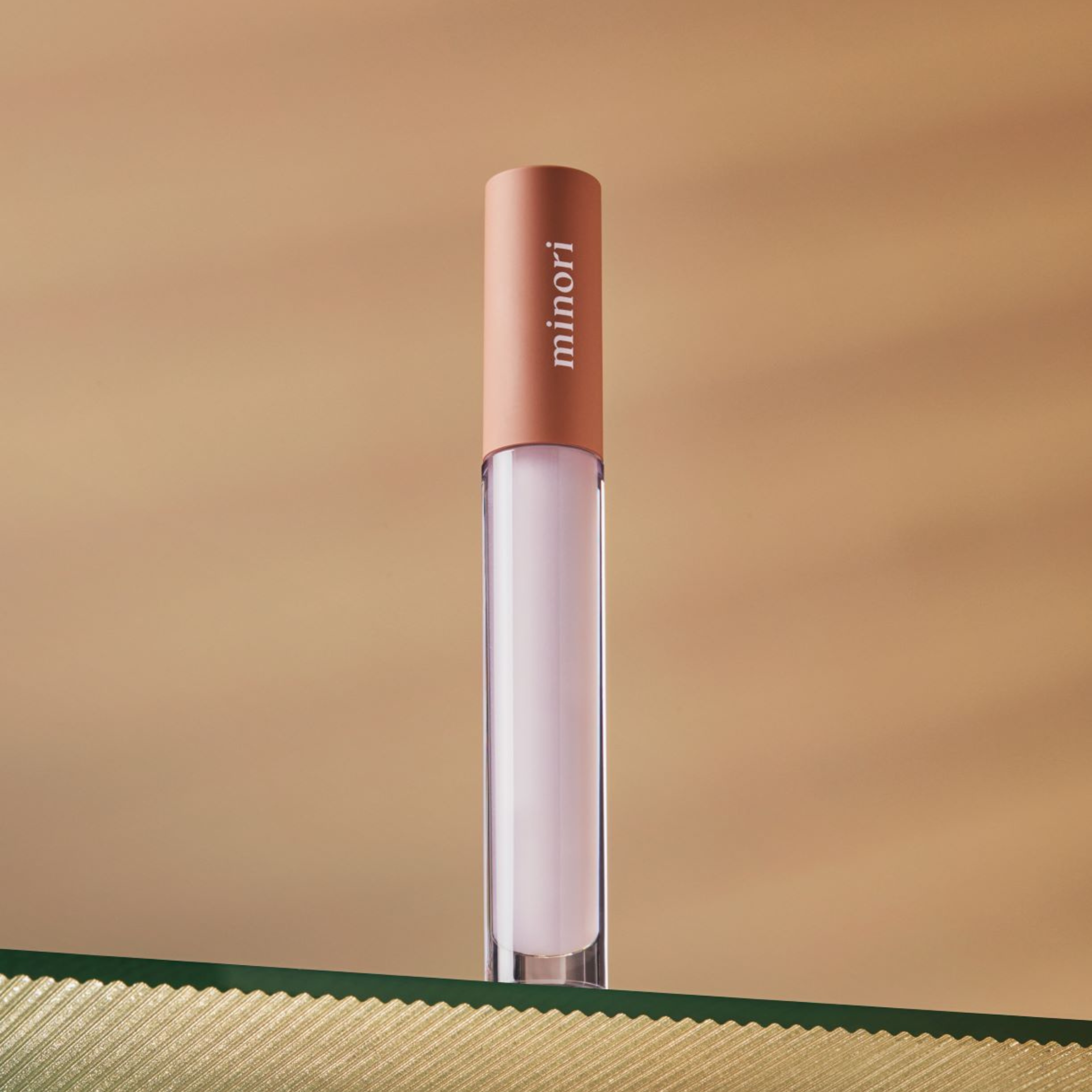 A tube of lip serum with a clear cap and a pink label, displayed against a soft-focus background.