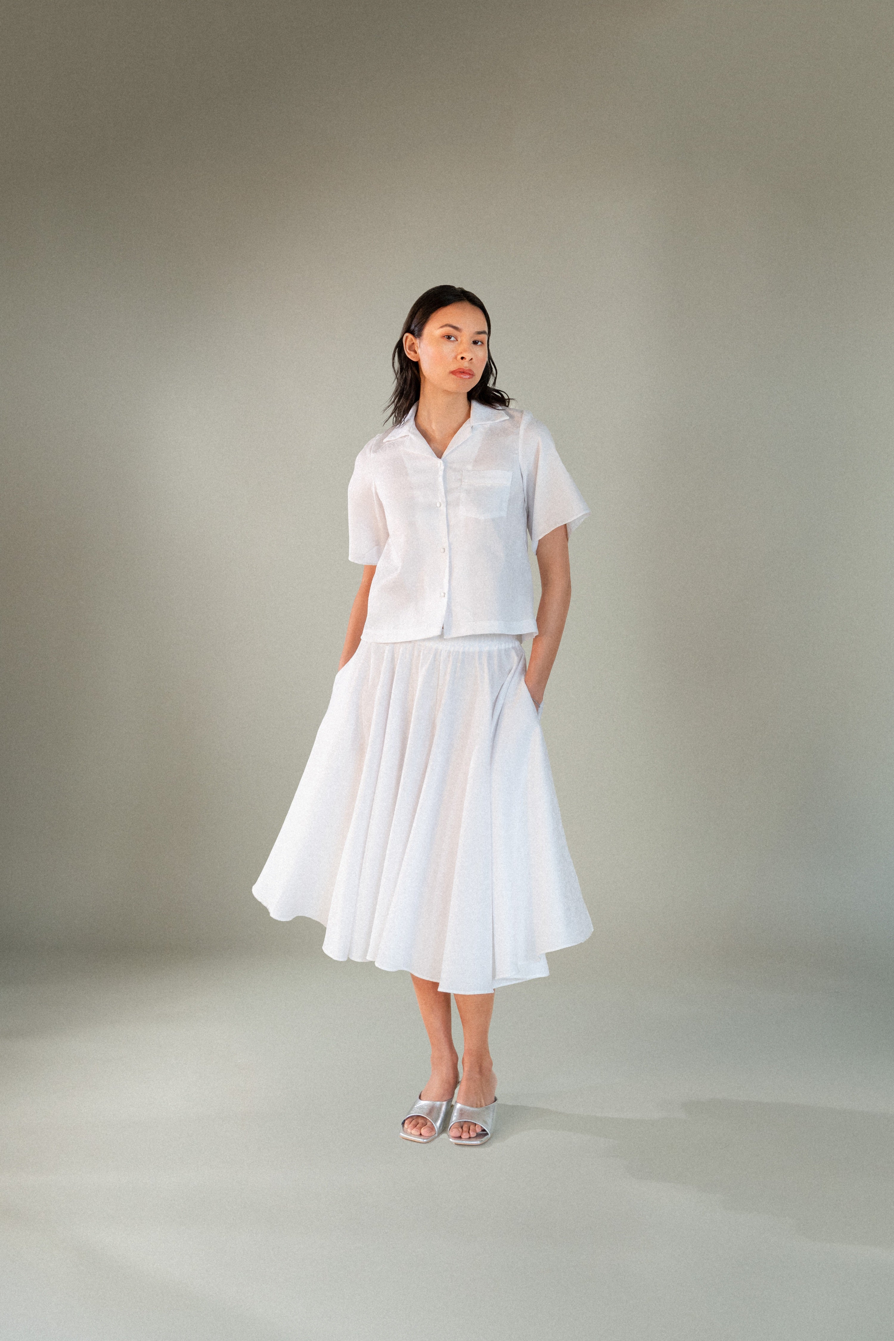 Woman wearing a white cotton midi skirt and white shirt against a plain background