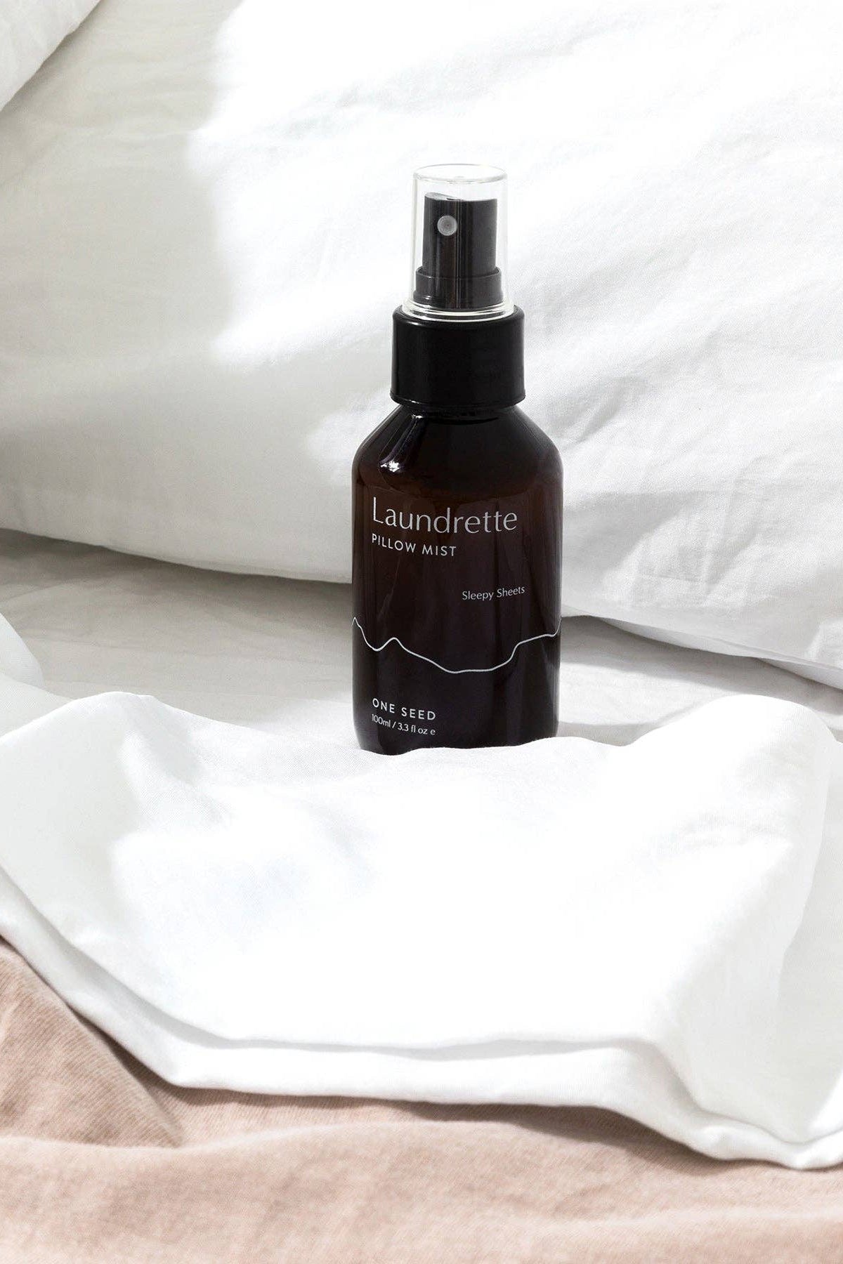 Laundrette pillow mist bottle on a white pillow and blanket