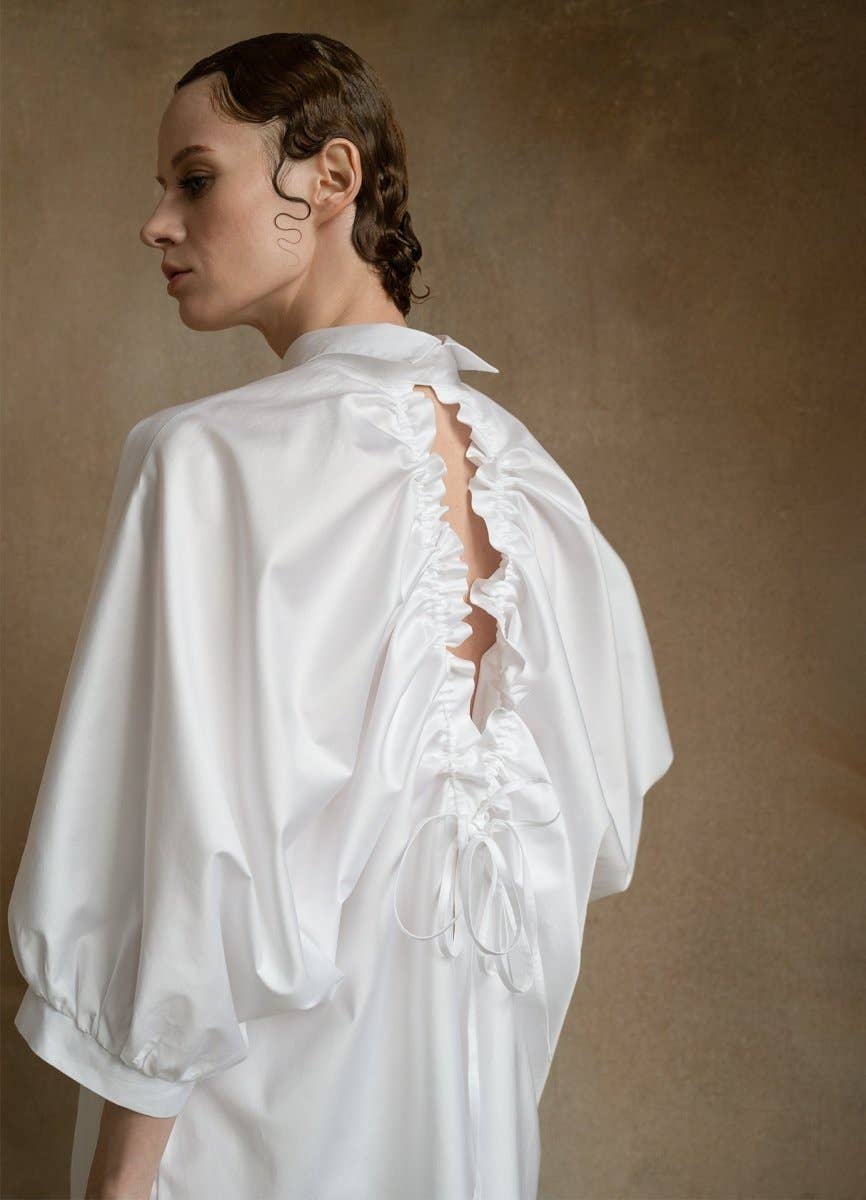 Woman wearing a white blouse with ruffled details on a brown background
