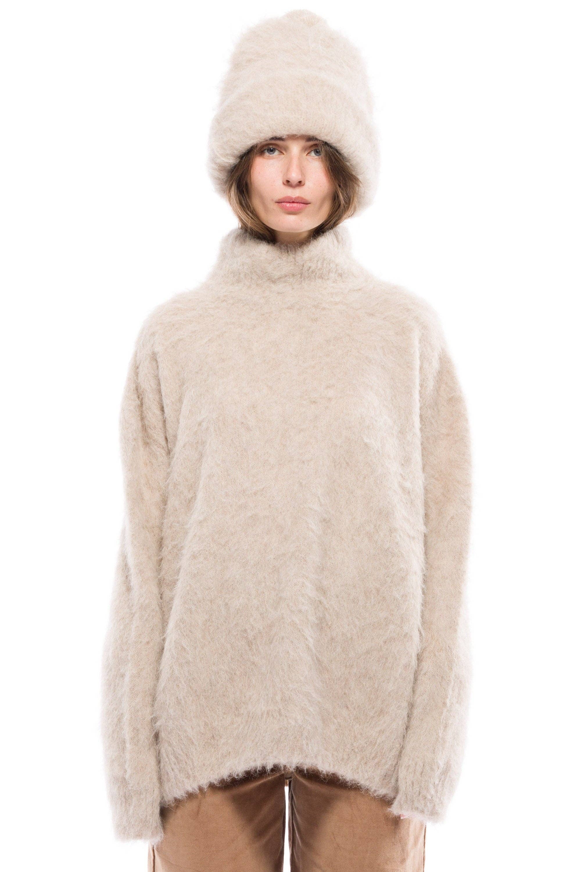 A person standing wearing a beige turtleneck sweater and brown pants.