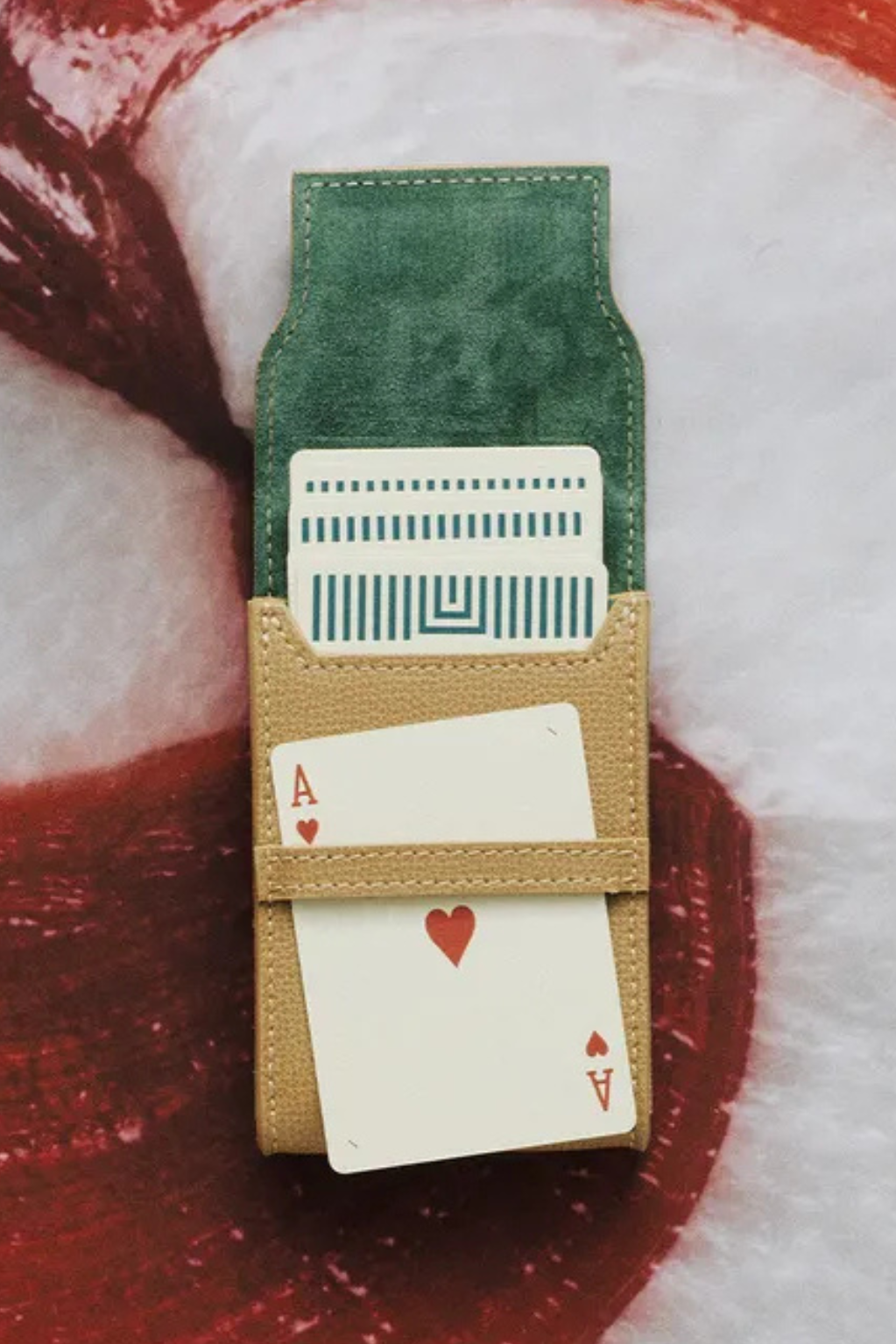 Playing cards in a green and beige card holder on a red and white background