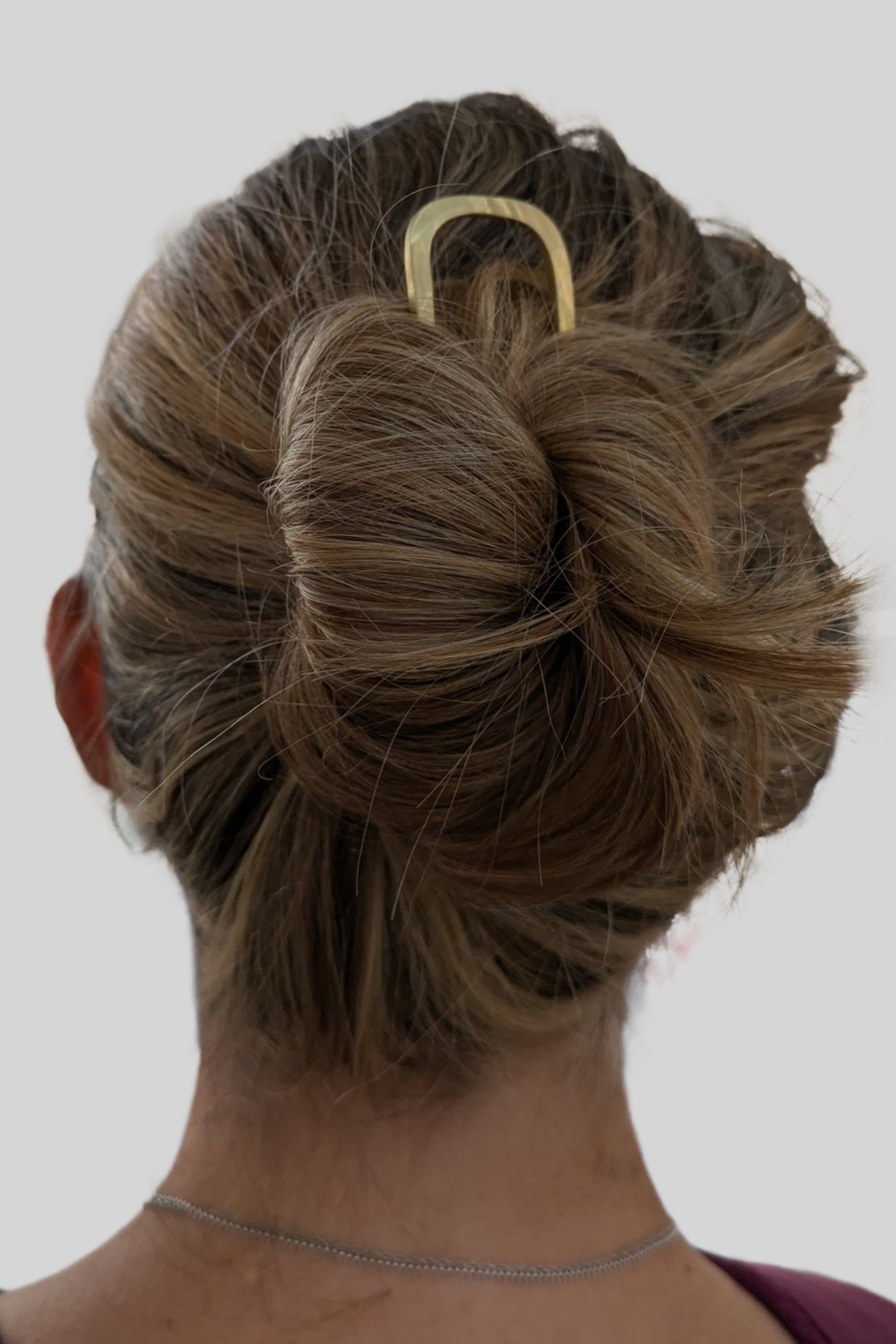 Back view of a person with styled hair and a hair clip on a plain background