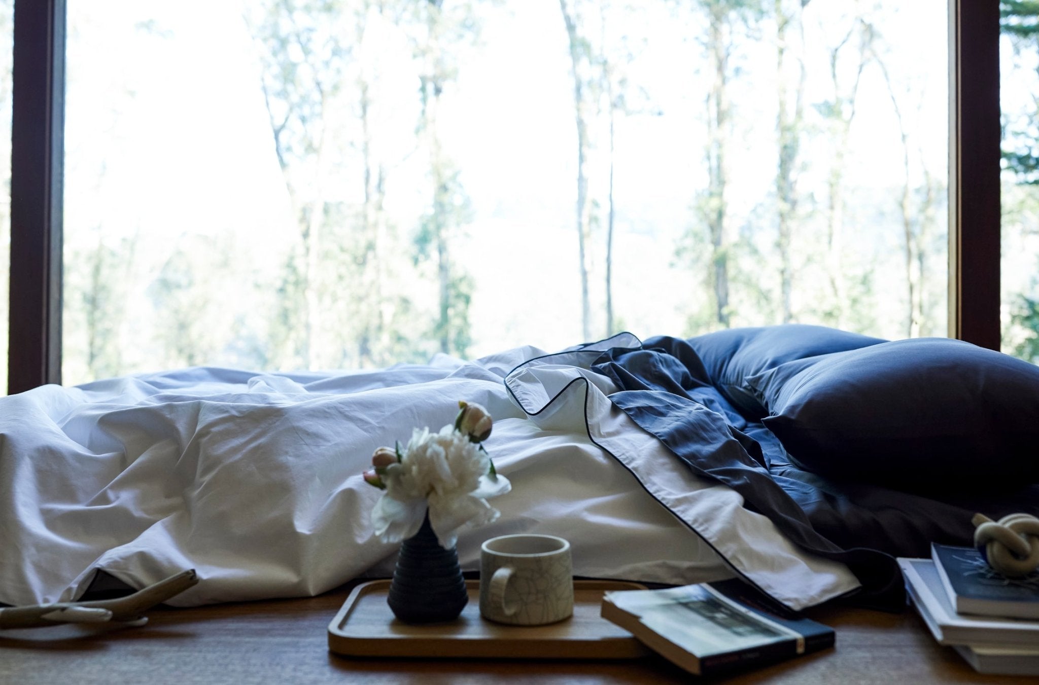 Bedroom with a bed, tray with items, and large windows showing trees.