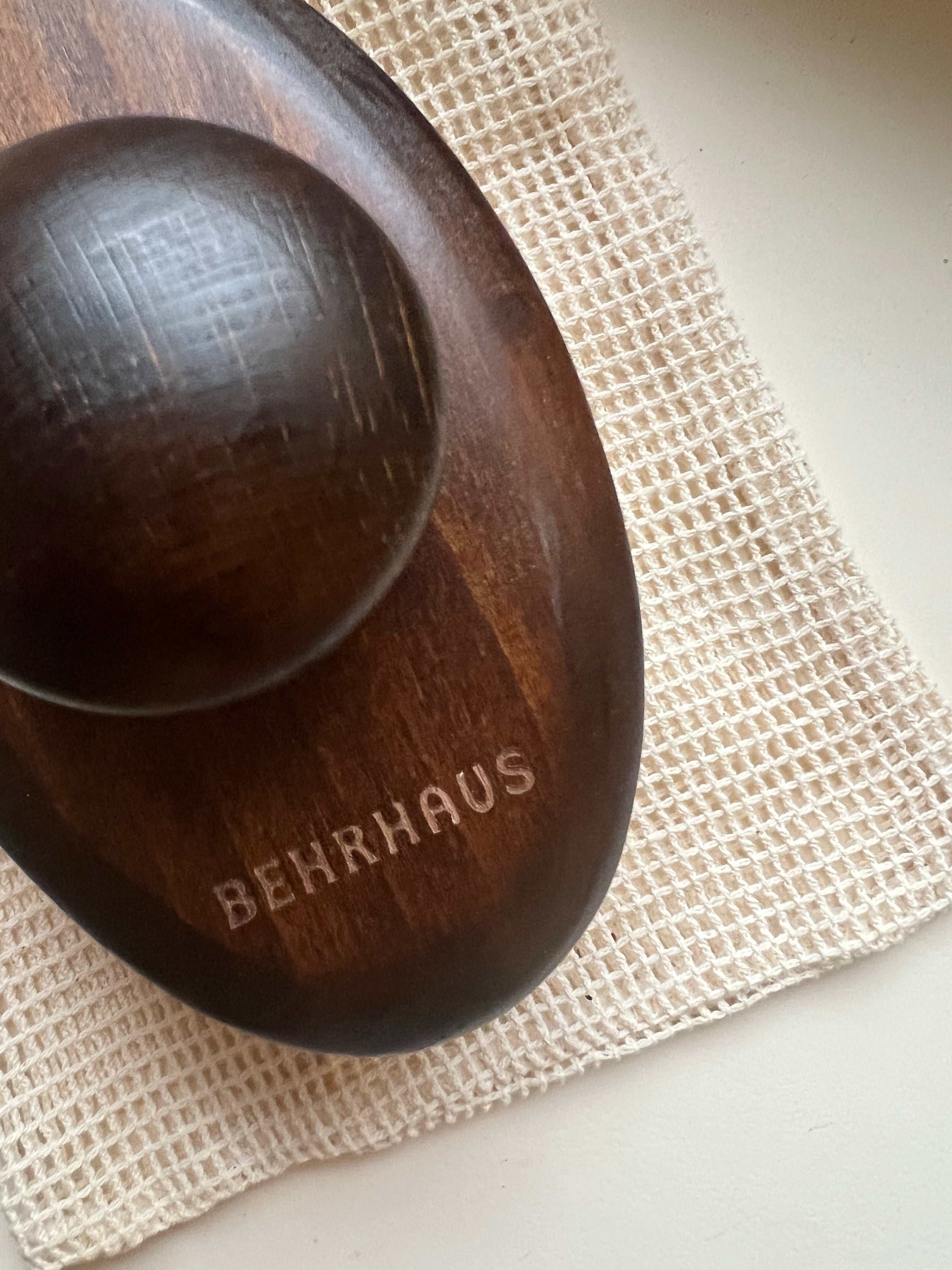 Wooden bowl with 'BEHRHAUS' engraving on a textured surface