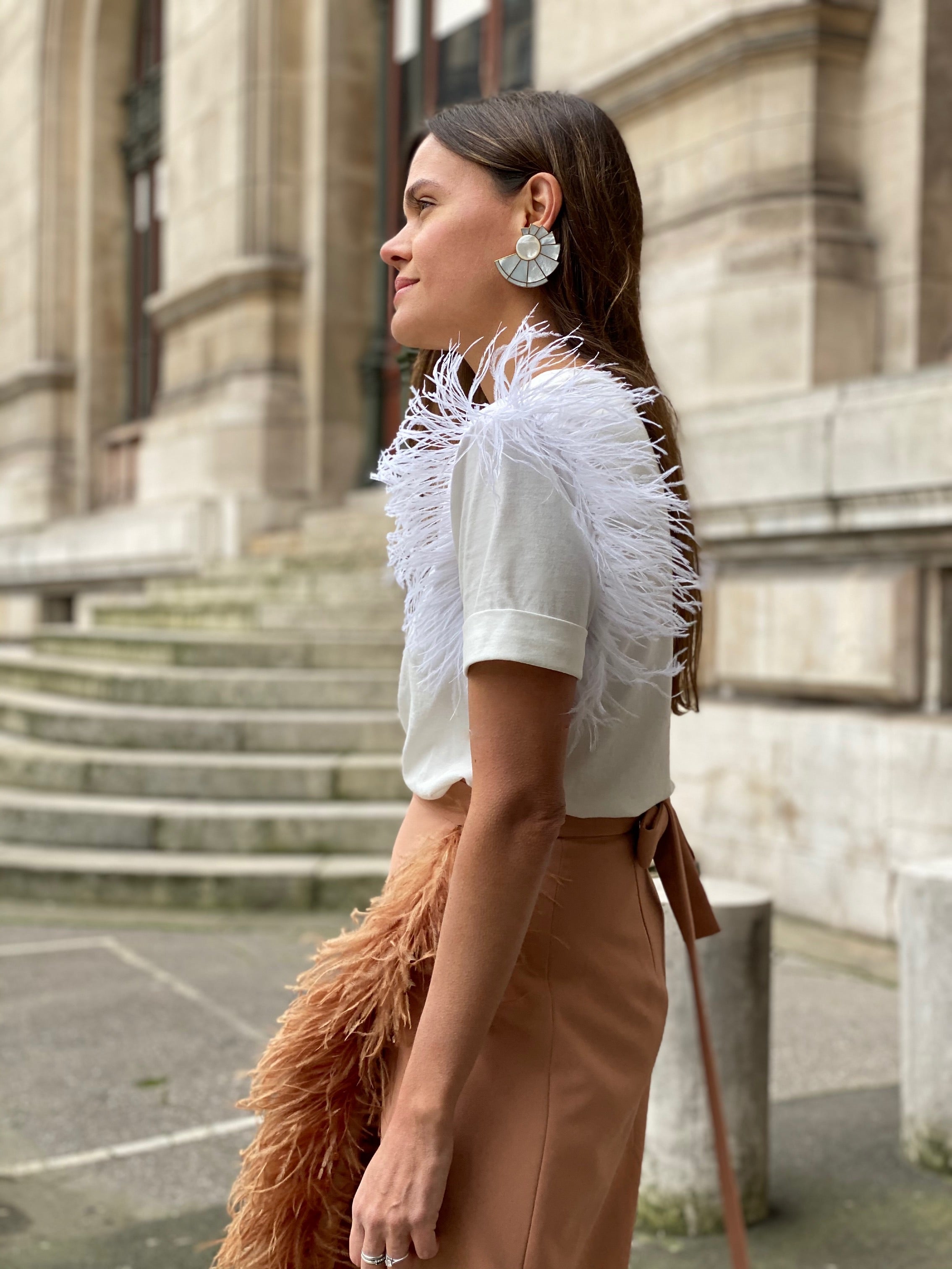 Woman wearing a white feathered top and brown skirt in front of a building.