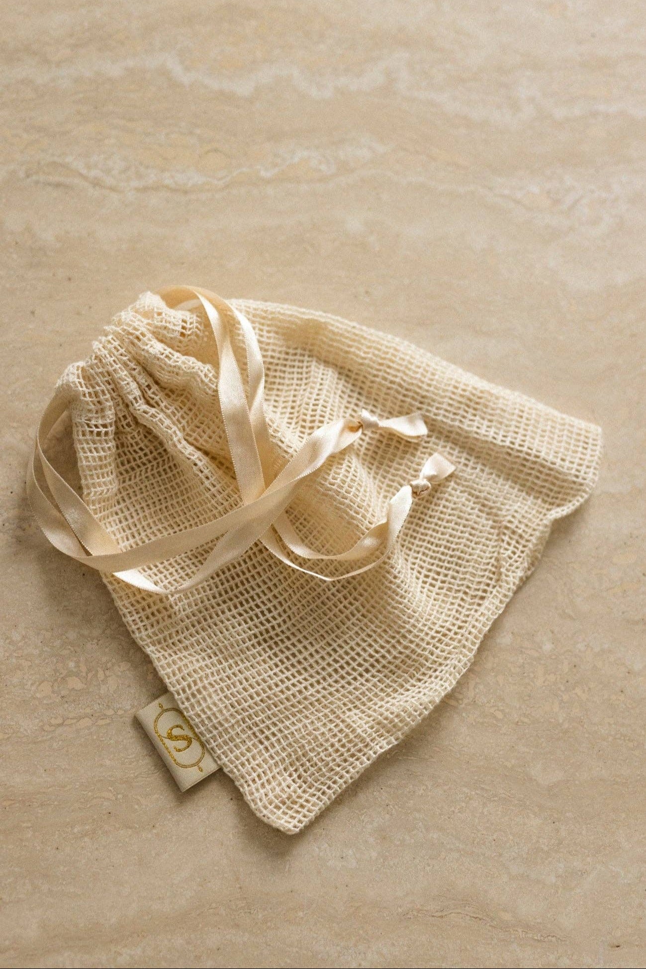 Beige mesh bag with drawstring on a beige marble surface