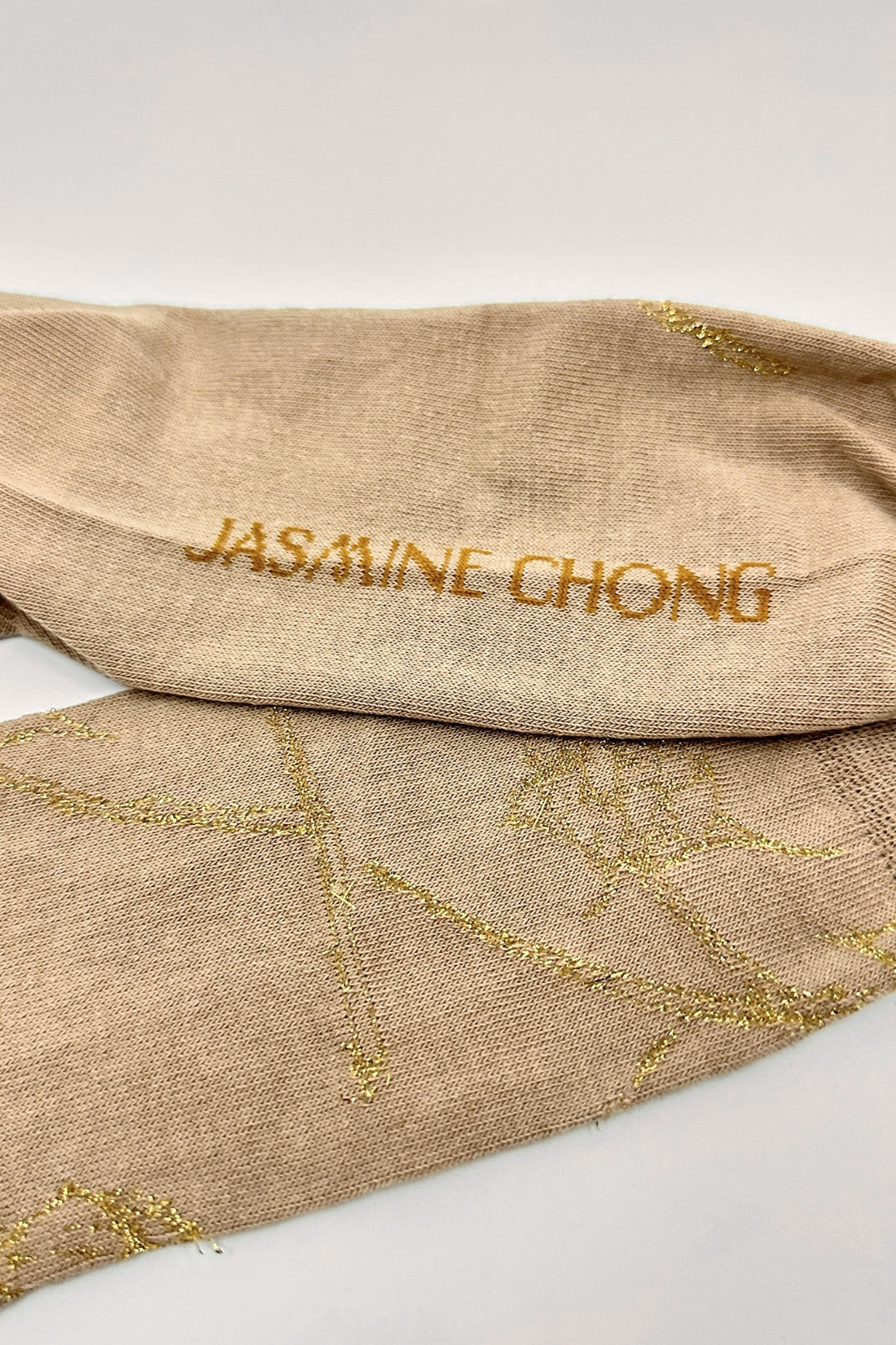 Beige fabric with gold embroidery and 'Jasmine Chong' branding on a white background
