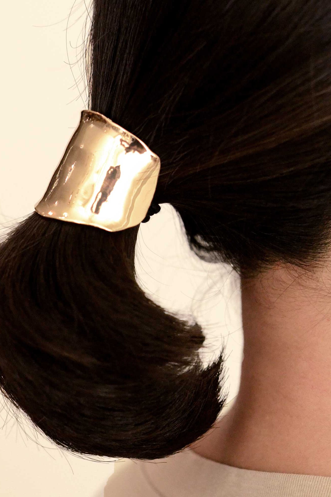 Gold hair tie on a bun against a neutral background