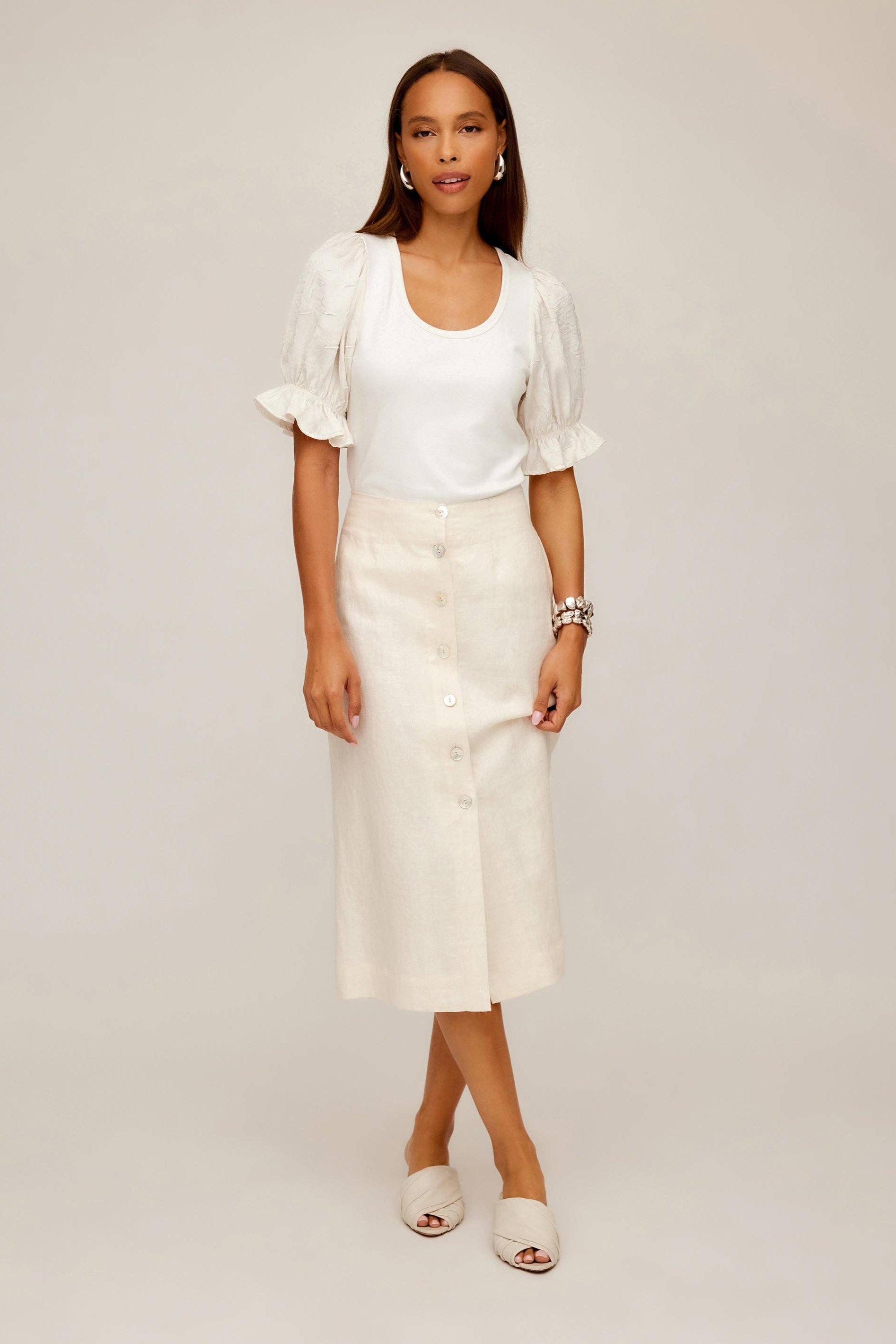 Woman wearing a white blouse and cream linen midi-length skirt against a plain background.