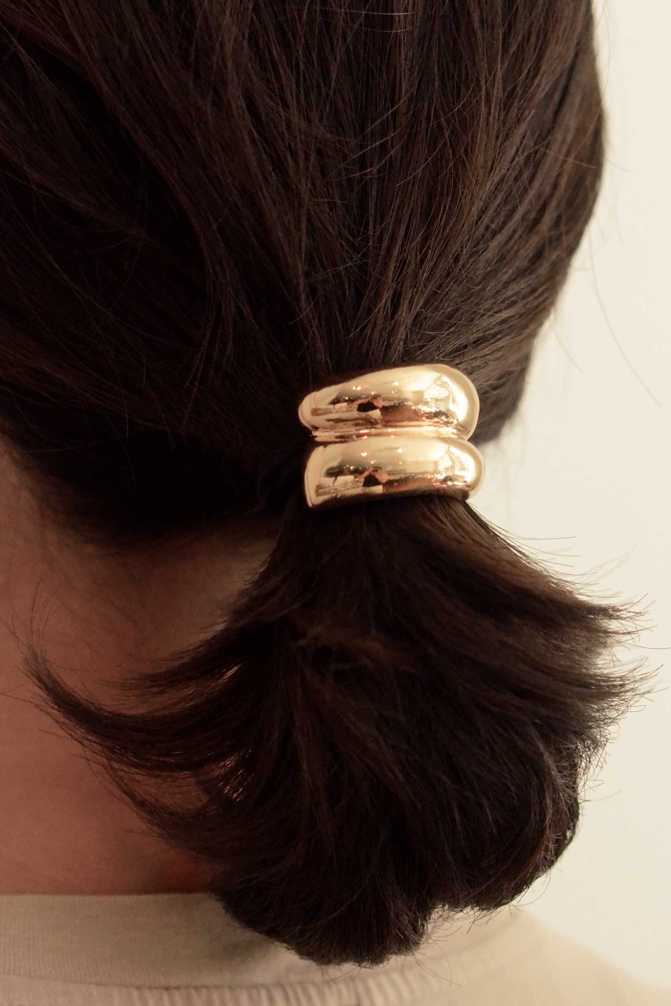Gold hair tie on a person's ponytail against a neutral background