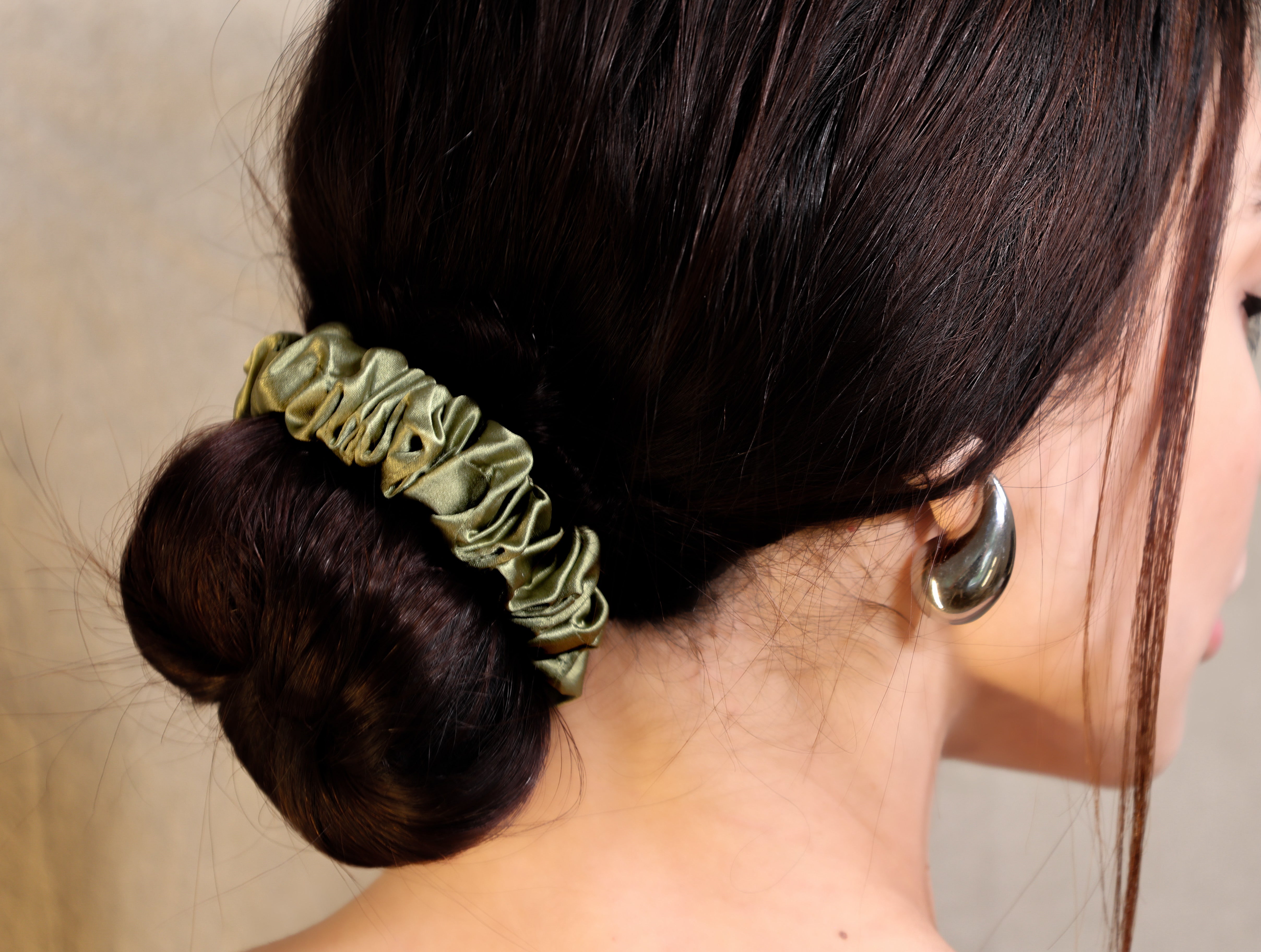 Woman with a bun holding a green scrunchie, wearing large hoop earrings.